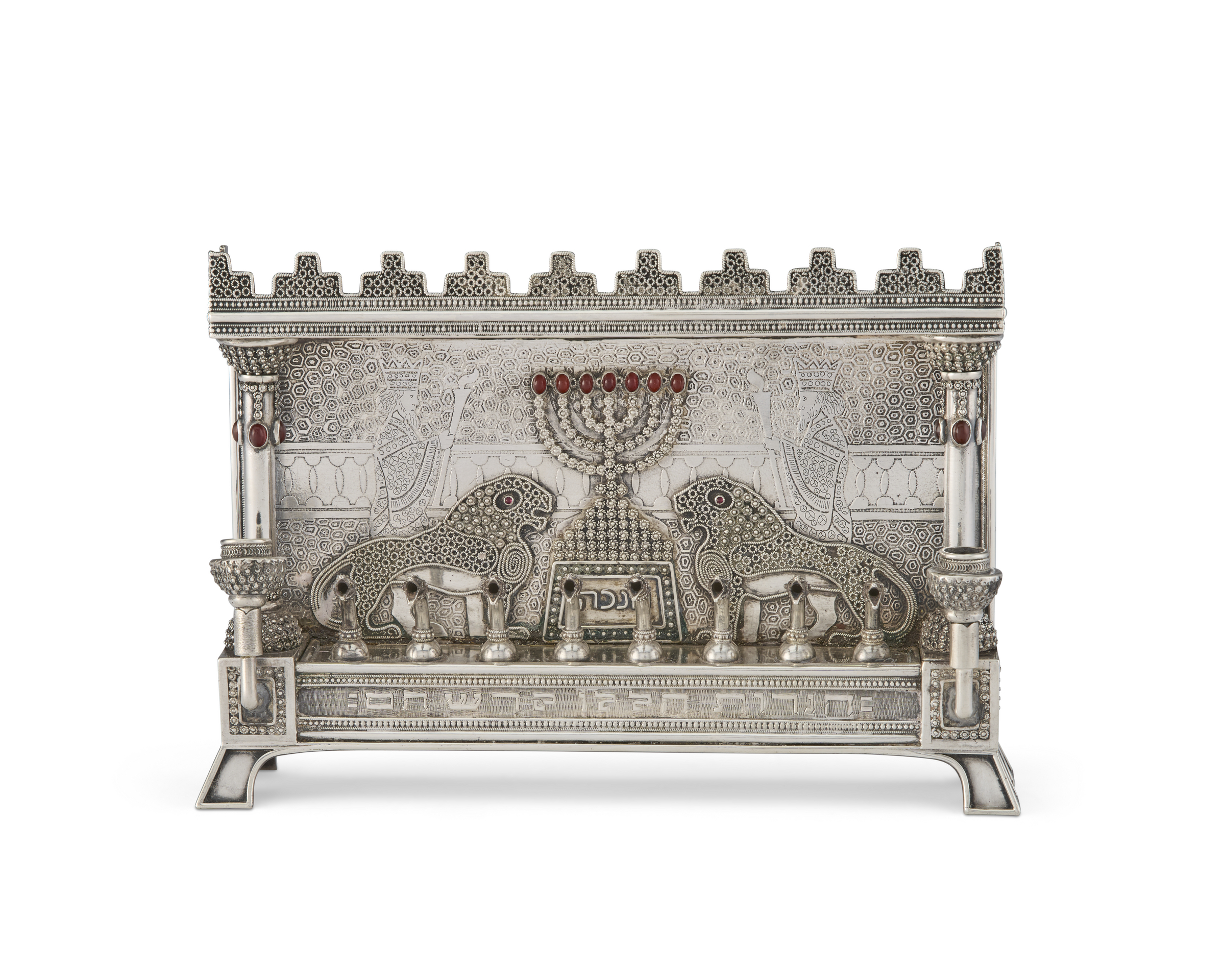 A decorative silver menorah with intricate designs, lions, columns, and red gem accents.