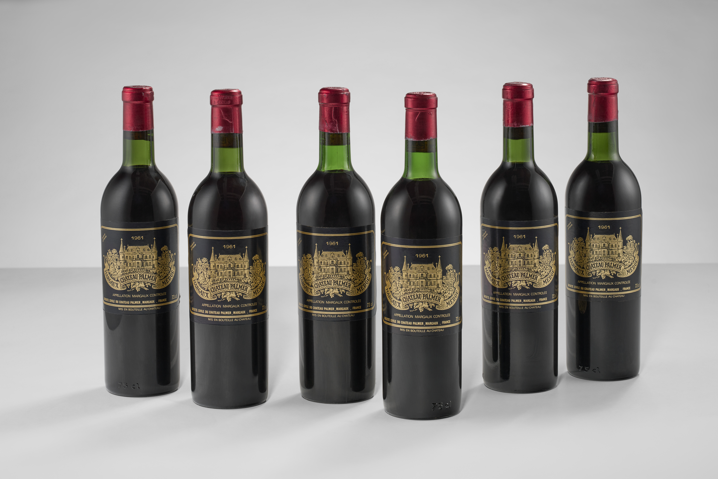 Six bottles of Château Palmer Margaux red wine from 1961 with gold and black labels and red foil caps are arranged in a row.
