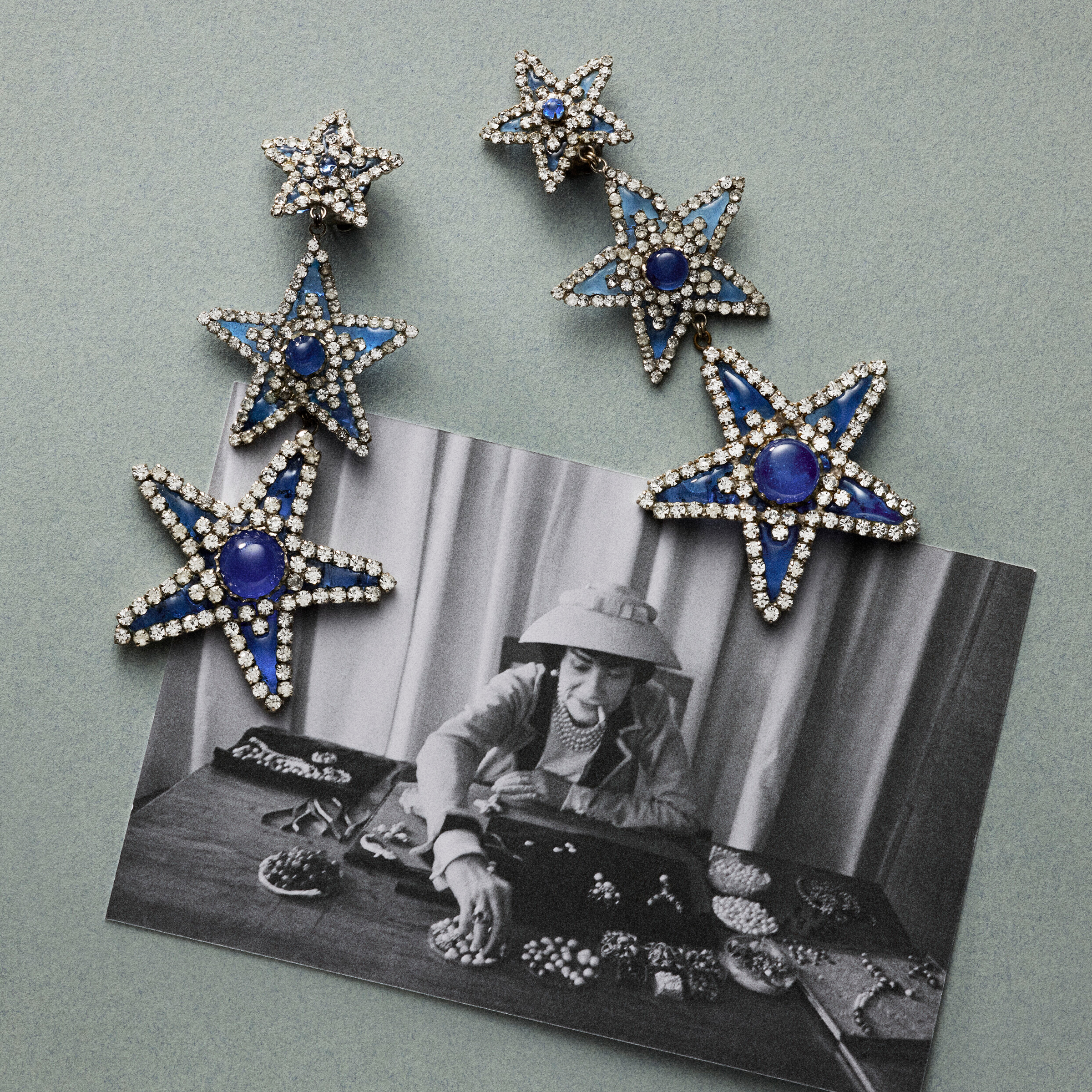 Five star-shaped rhinestone and blue jeweled brooches rest on a black-and-white photo of a person organizing jewelry on a table.