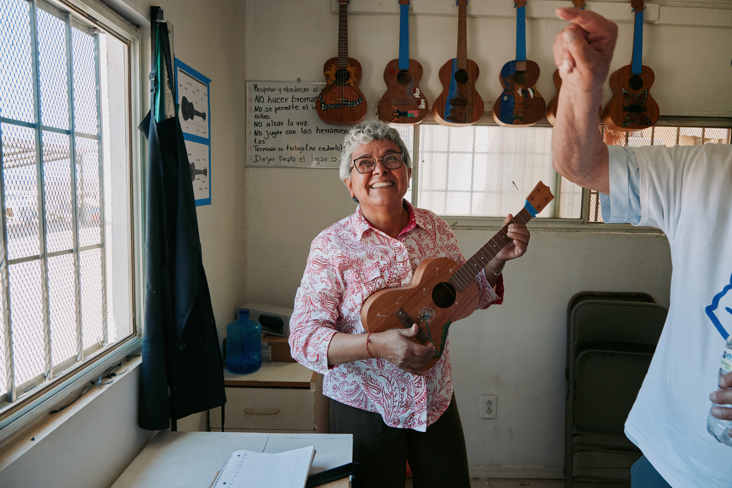 A person is holding a guitar in a room with several guitars hanging on the wall.