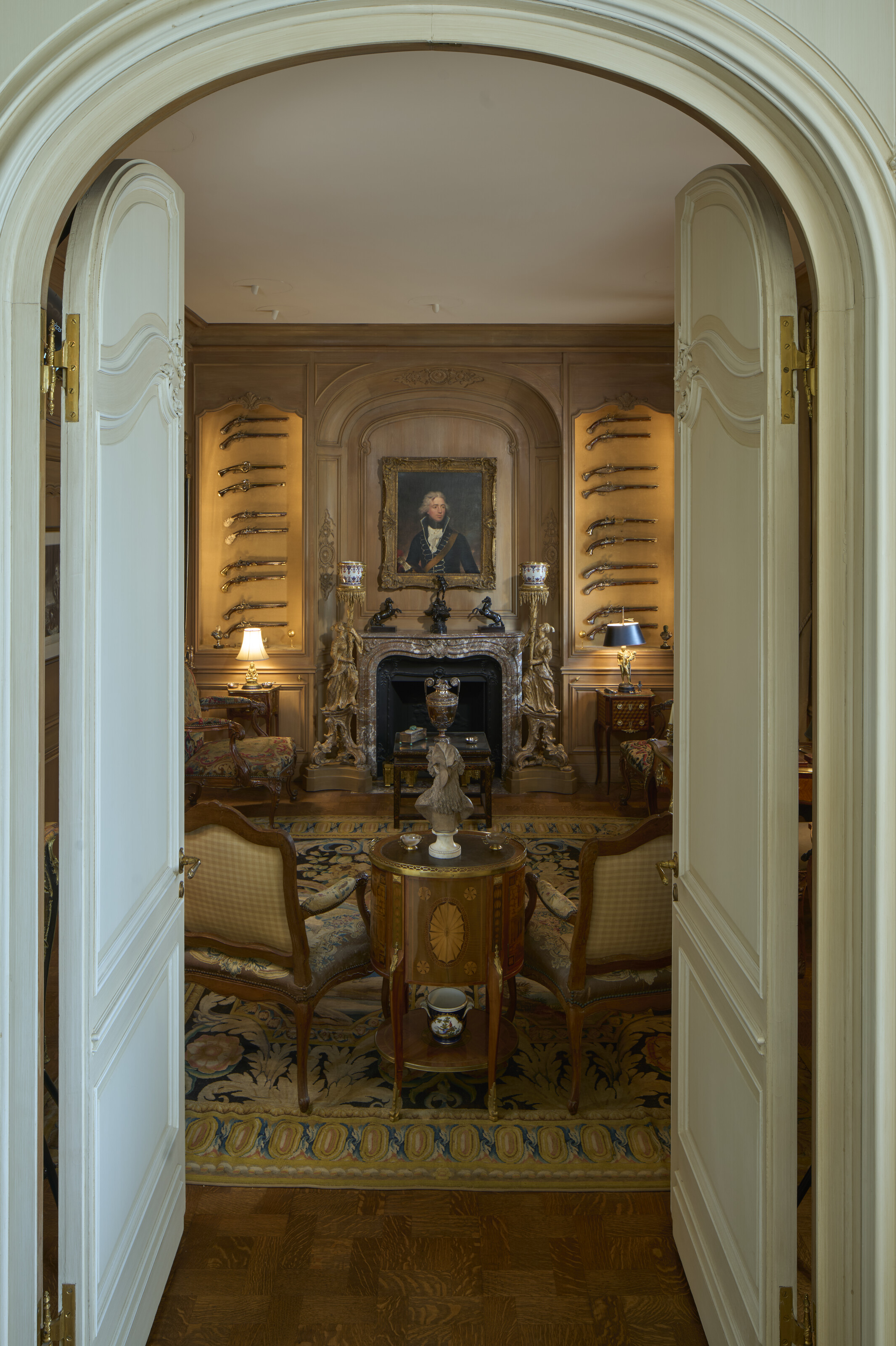 An elegant room with antique furniture, ornate decorations, and a fireplace beneath a portrait.