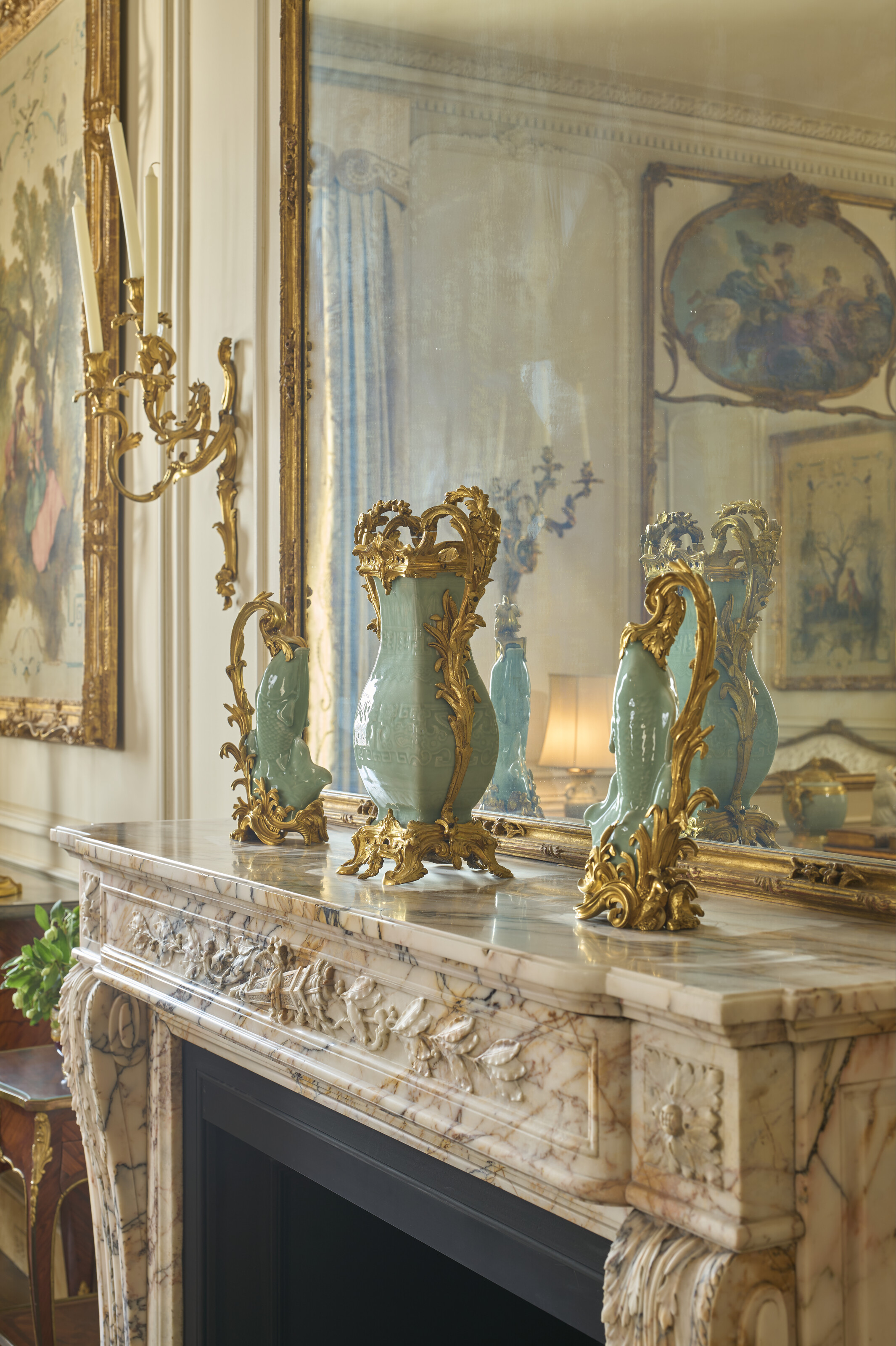 A marble fireplace mantel with ornate vases and a large mirror in an elegant room.