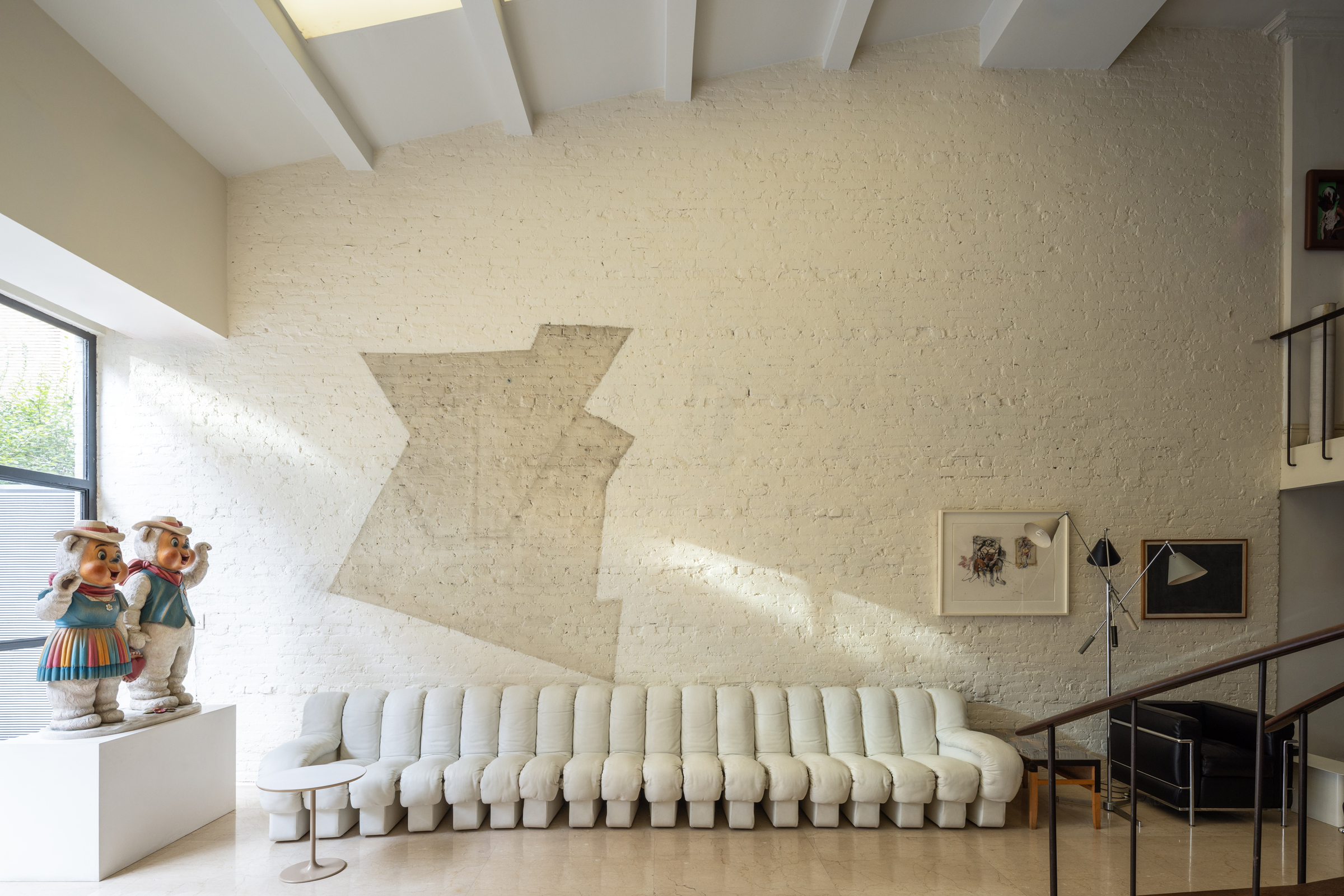 A modern living room with a long tufted sofa, wall art, and two large character statues.