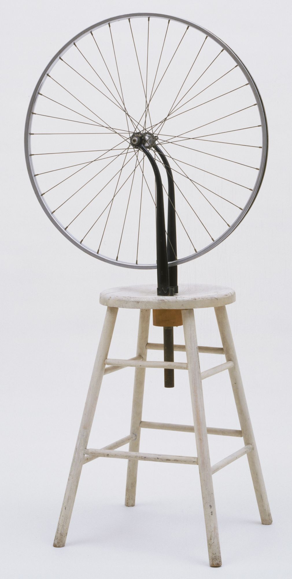 A bicycle wheel is mounted upside down on top of a simple wooden stool.