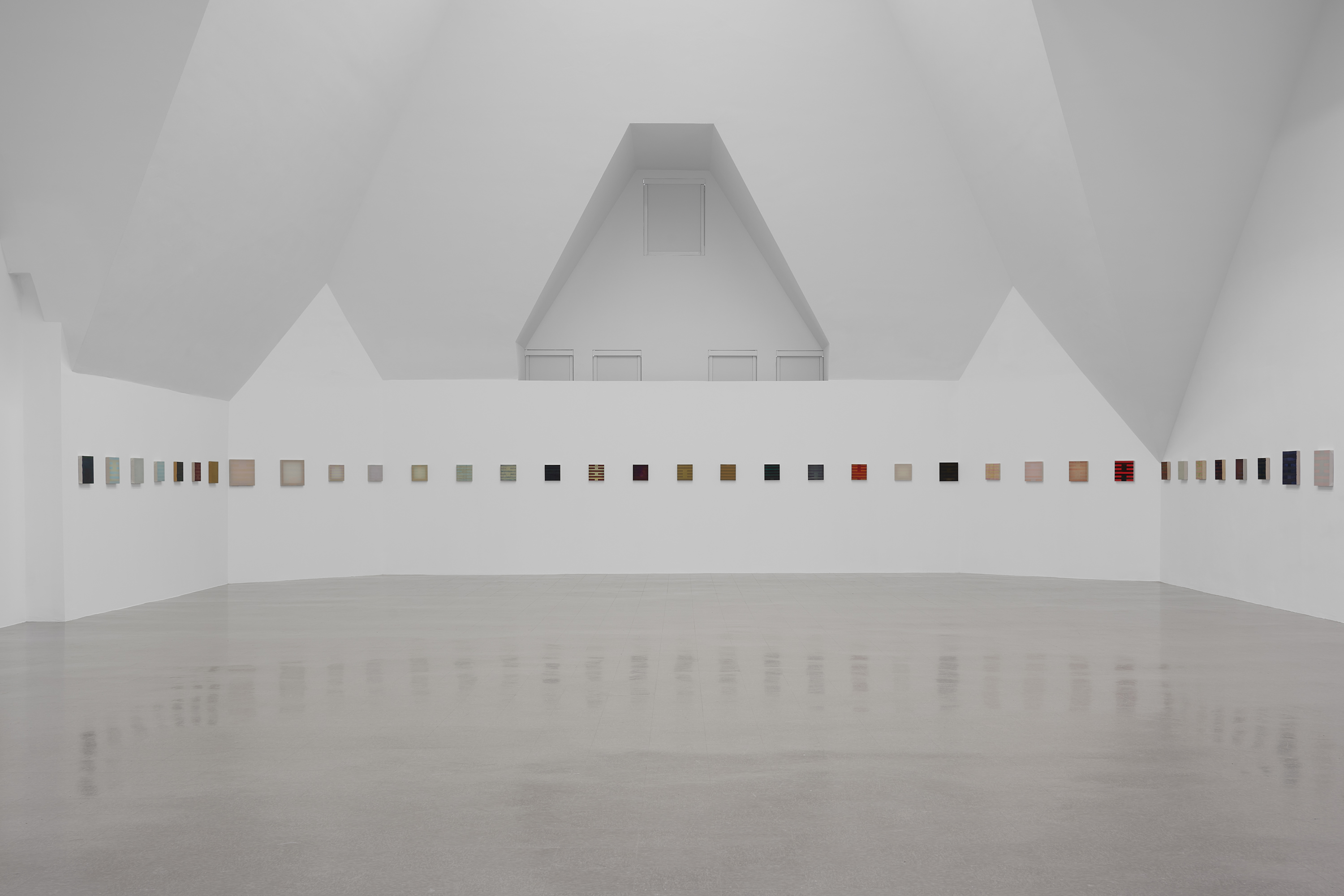 A minimalist gallery displays small rectangular artworks evenly spaced along white walls.