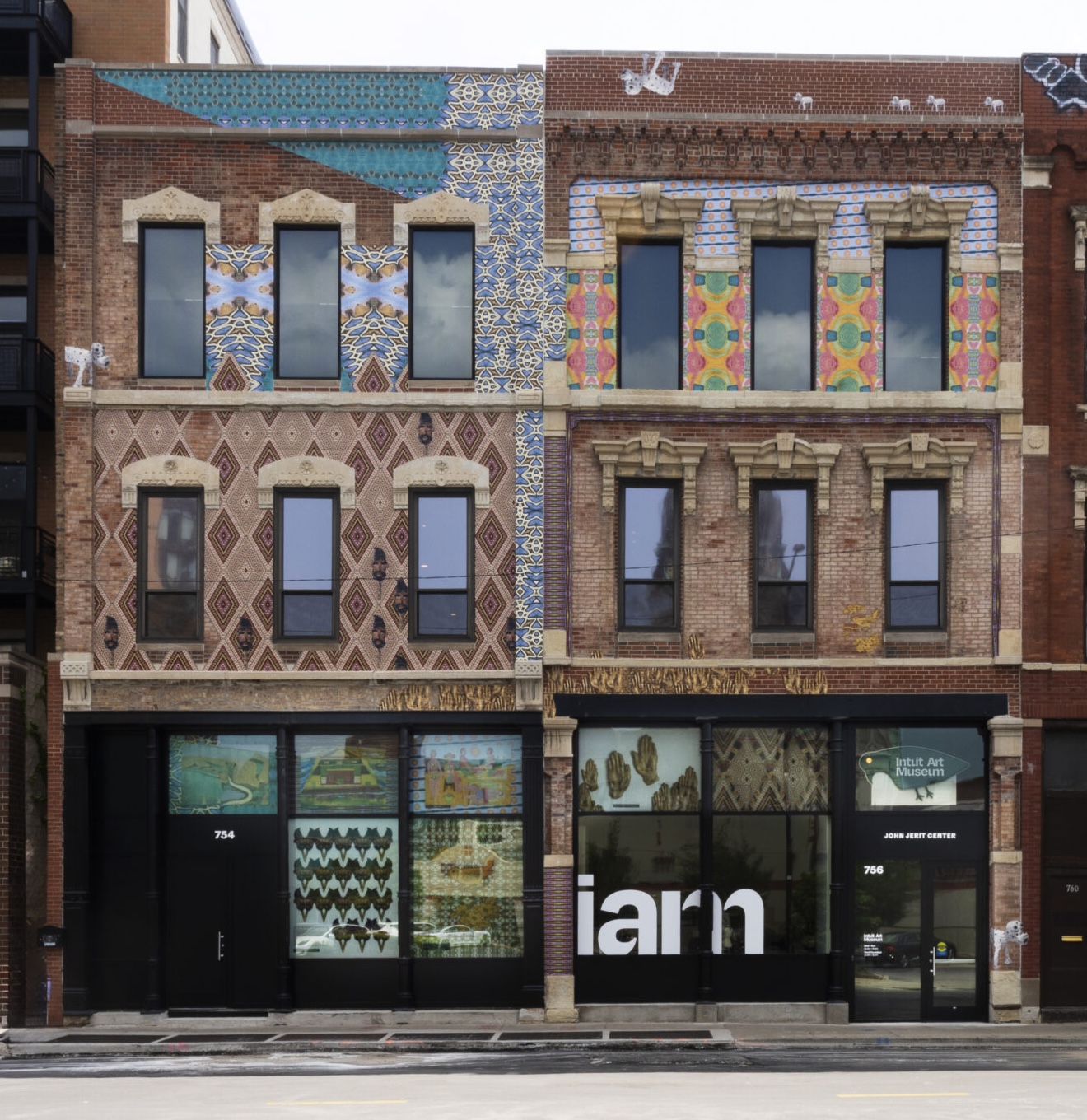 A brick building with colorful geometric murals and large “iam” lettering on the glass entrance.