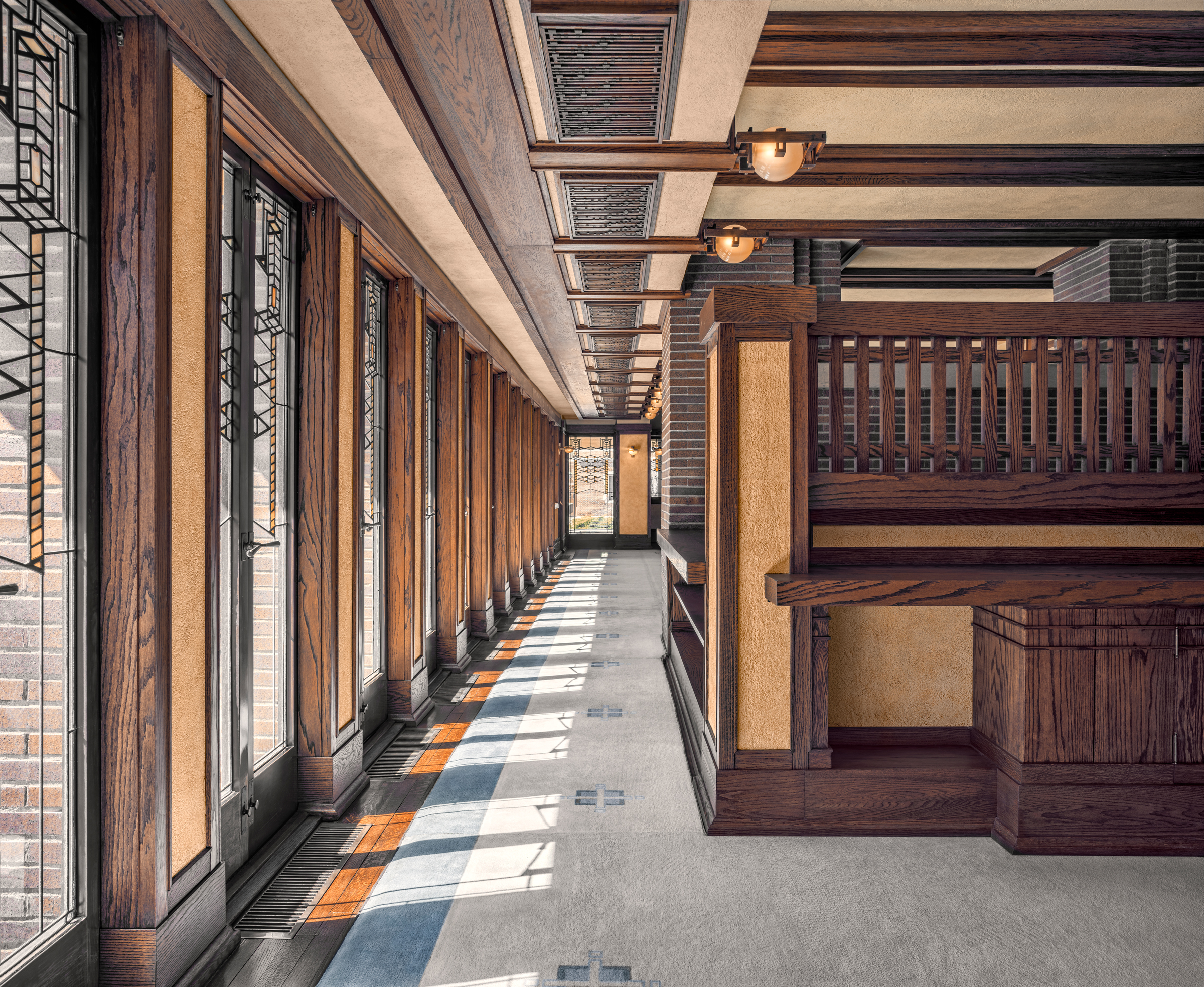 A hallway with stained glass windows, wooden beams, and sunlight streaming onto the floor.