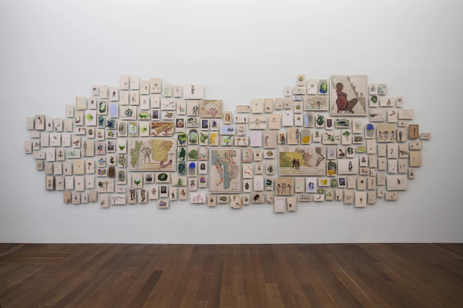 Many small framed artworks are arranged in a cloud shape on a white gallery wall.