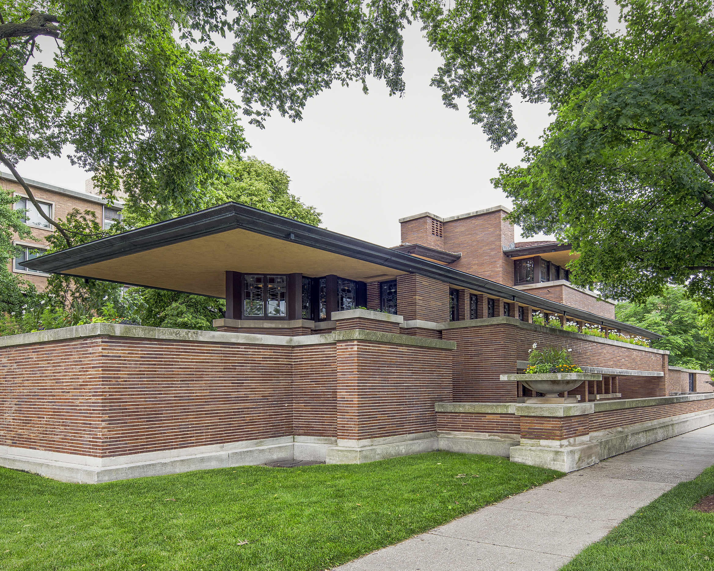A modern brick house with flat overhanging roof and geometric lines surrounded by trees.