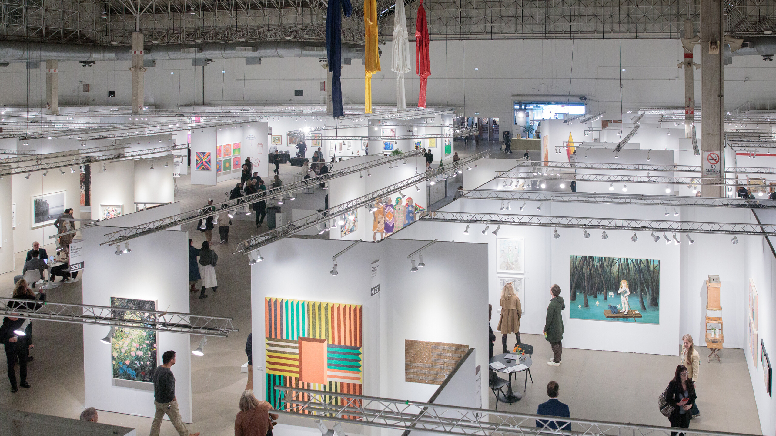 People are viewing artworks at a large, modern indoor art exhibition or gallery event.