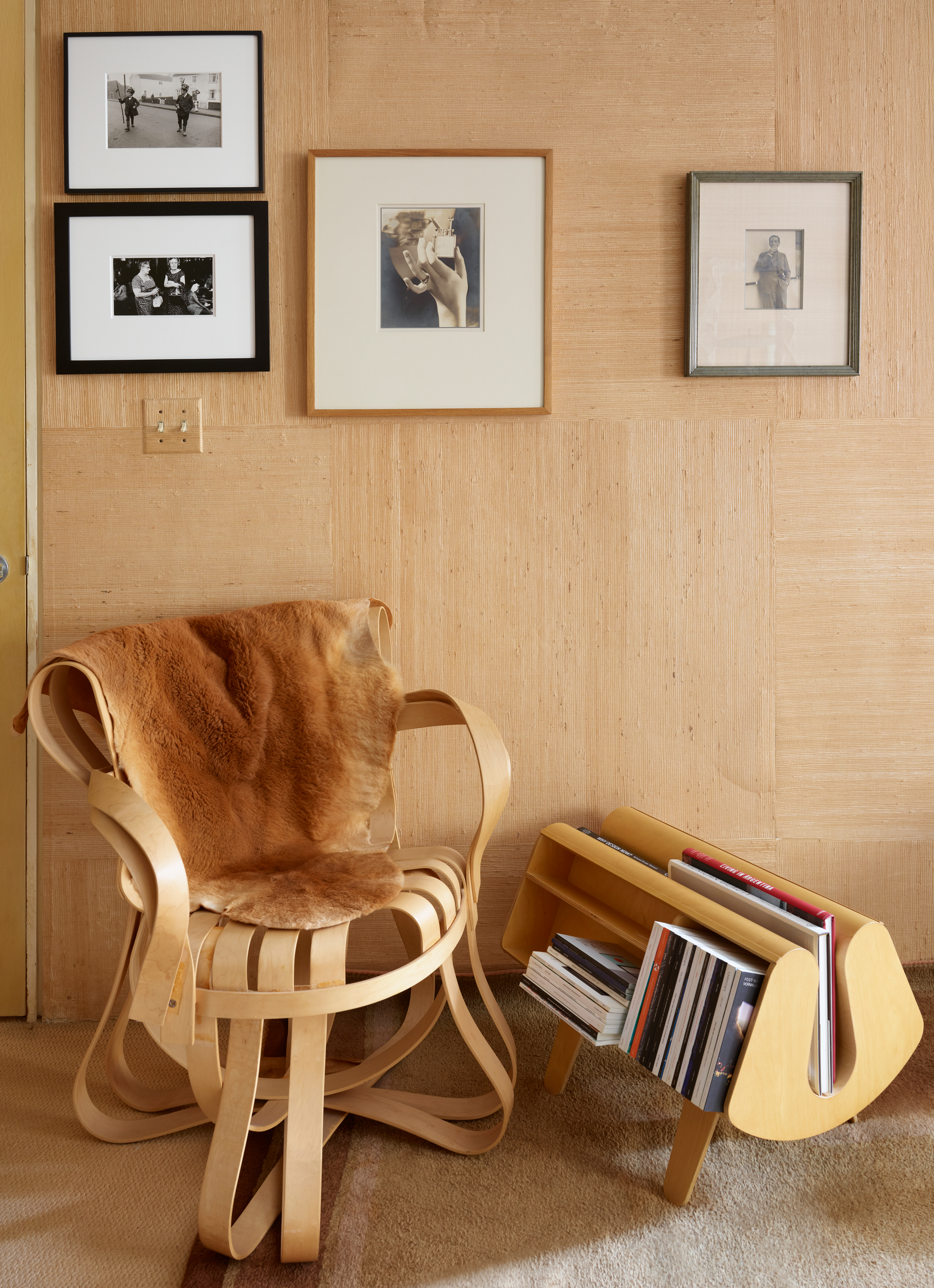 A cozy corner with a wooden chair, fur throw, magazine rack, and framed photos on the wall.