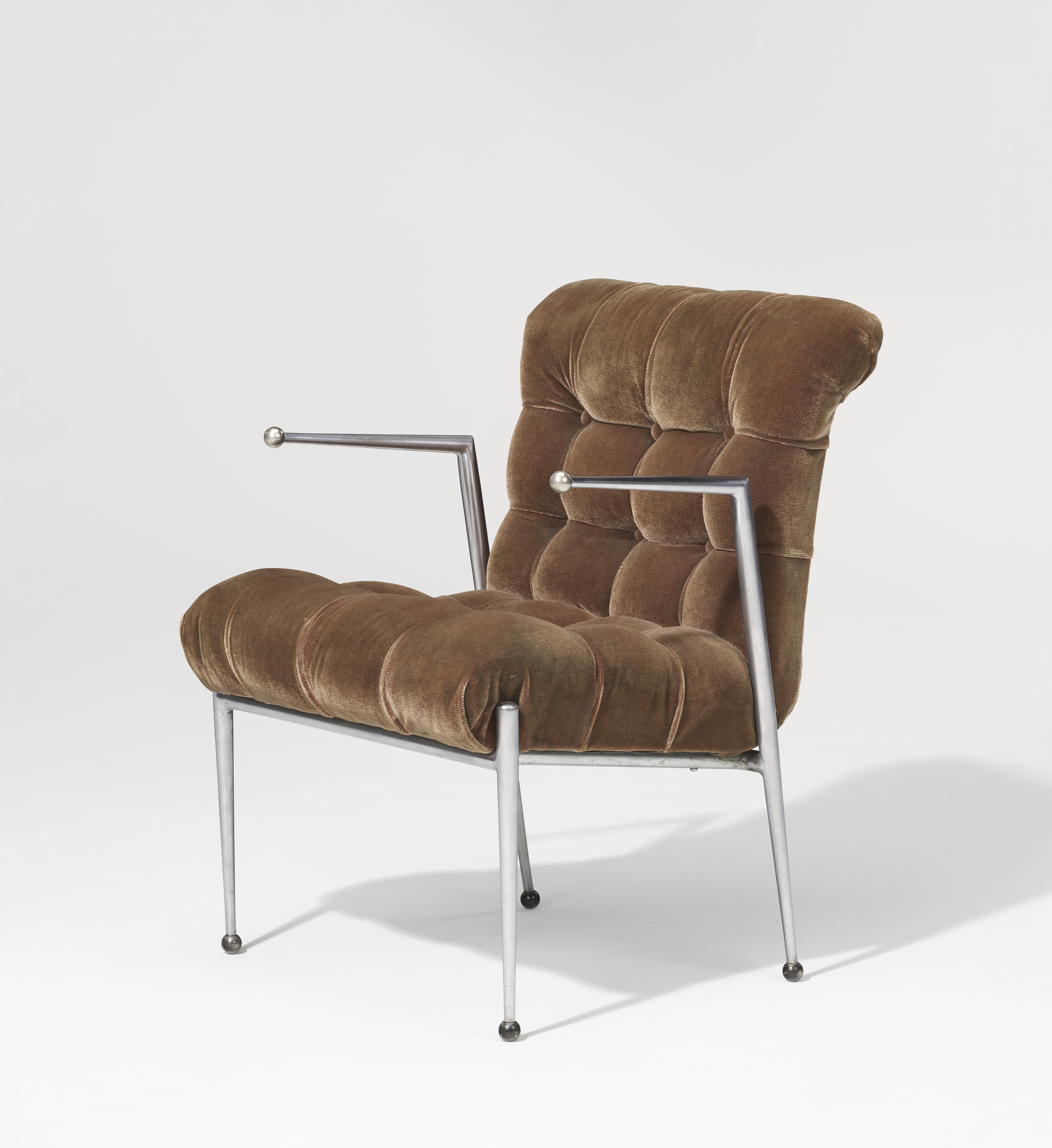 A brown tufted velvet chair with metallic frame and ball-tipped armrests.