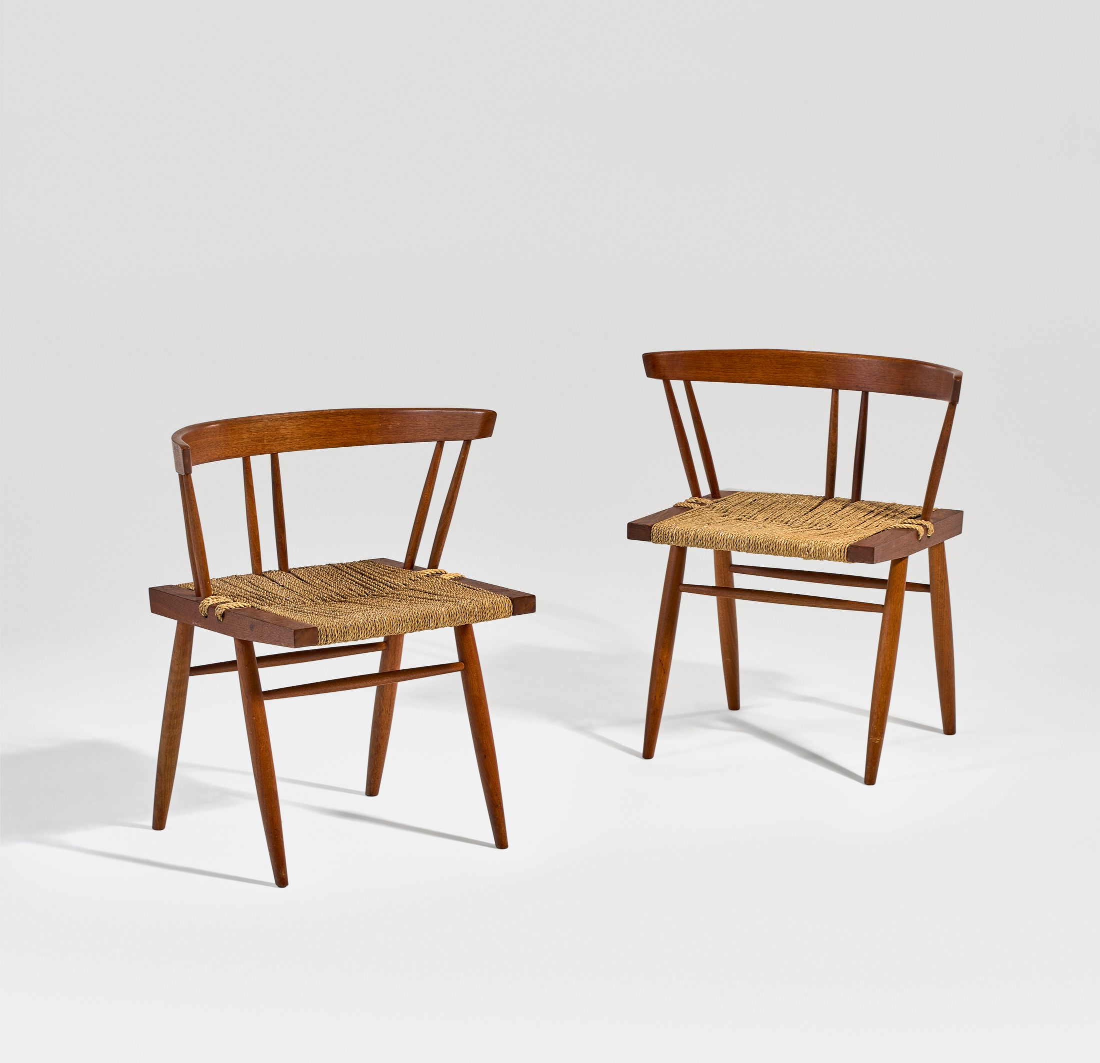 Two wooden chairs with woven seats and curved backrests are placed against a plain background.