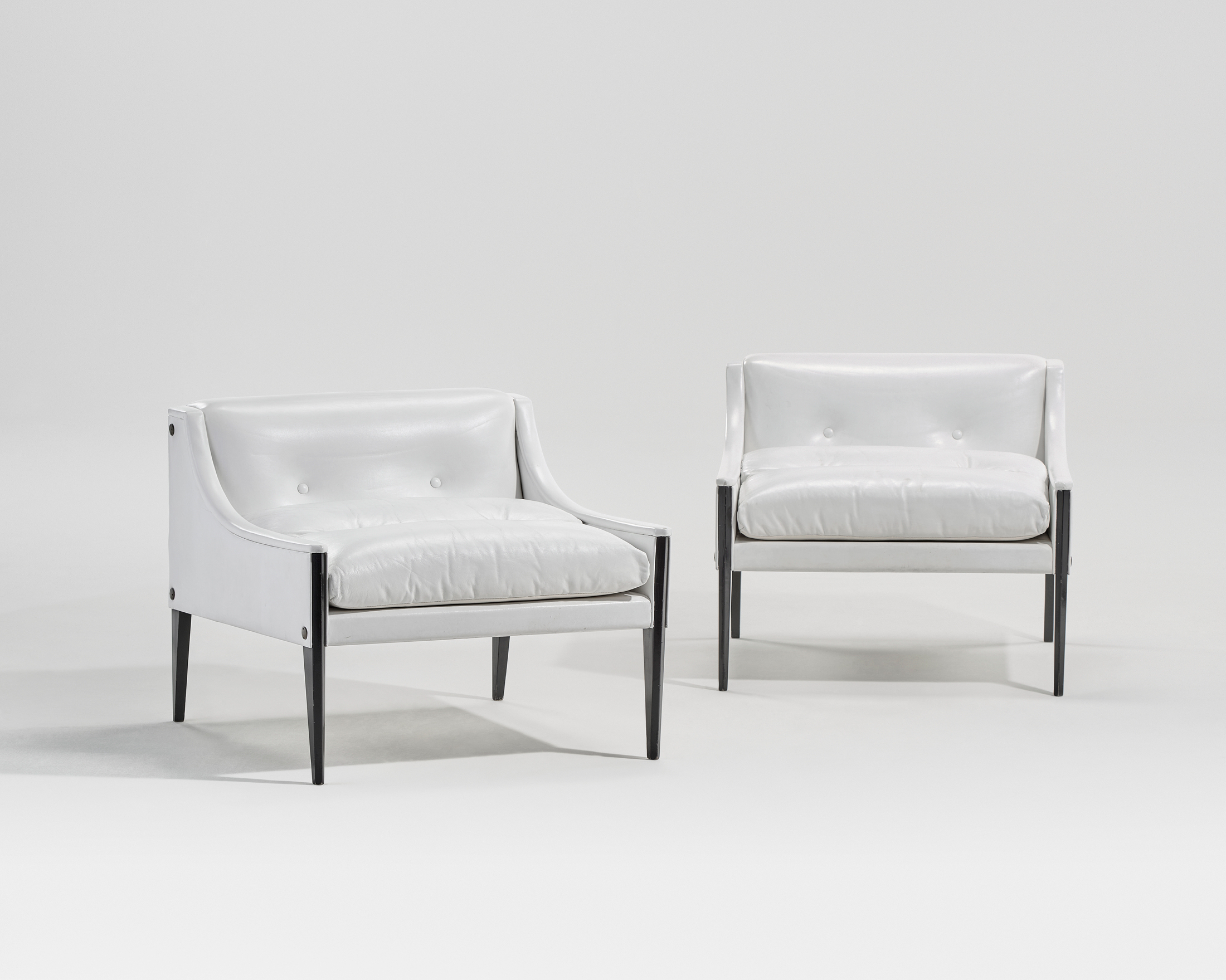 Two modern white armchairs with black legs are placed side by side against a plain background.