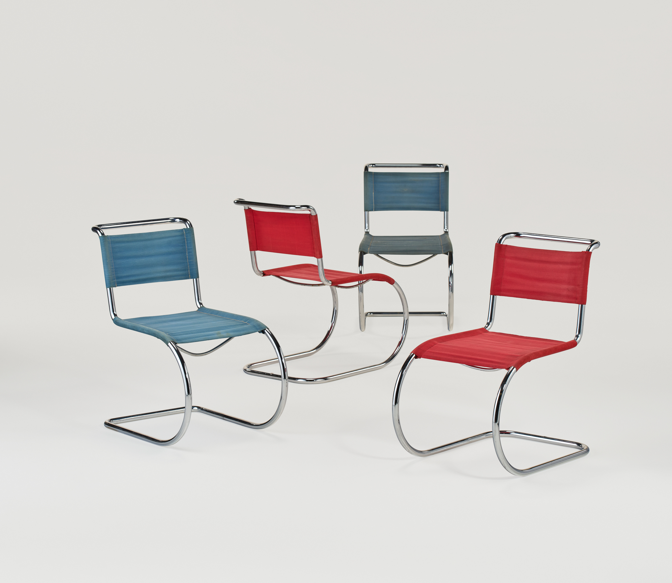 Four modern chairs with chrome frames and red or blue seats are arranged on a white background.