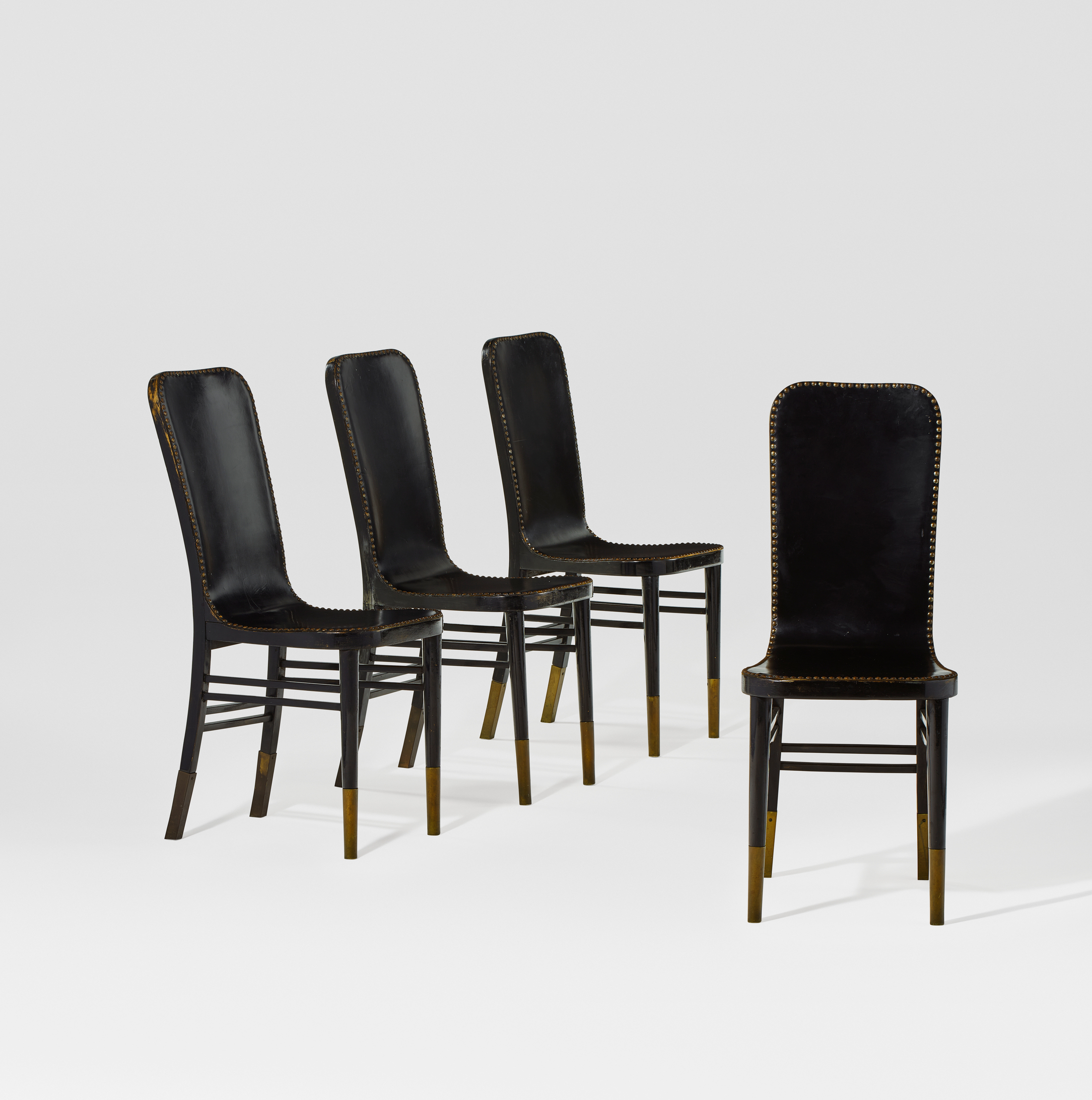 Four black leather chairs with brass accents are arranged against a plain white background.