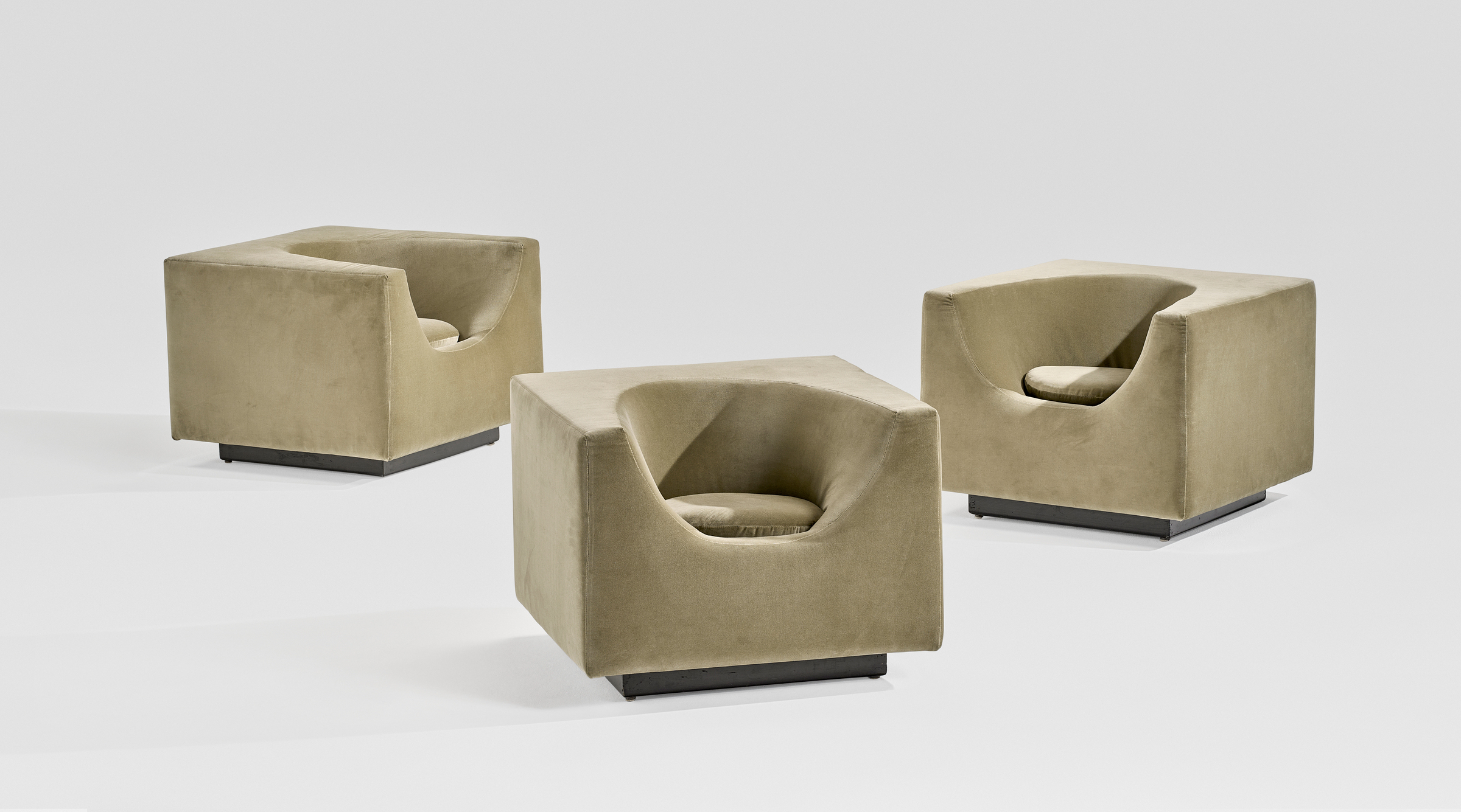 Three modern, cube-shaped beige armchairs with recessed seats are placed on a plain background.
