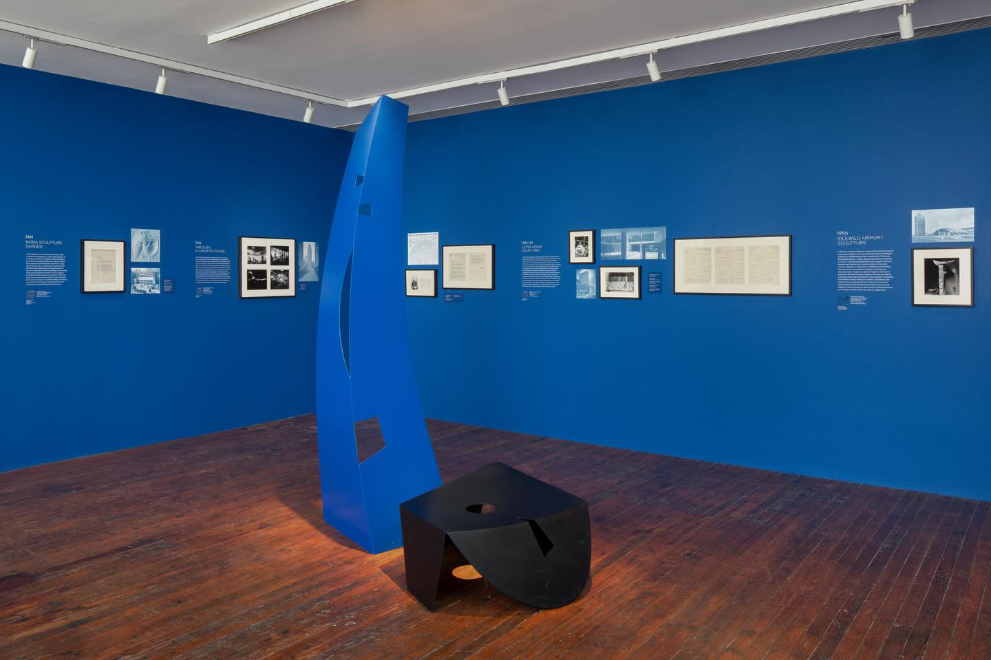 A modern art gallery with blue walls, framed artworks, and abstract blue and black sculptures.