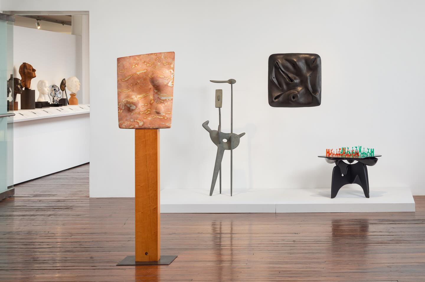 A modern art gallery displays abstract and sculptural artworks on white walls and wooden floors.