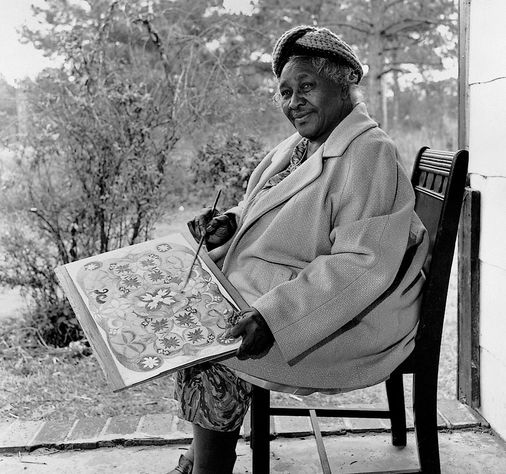 A person sits on a chair outside, painting colorful flowers and patterns on a canvas.