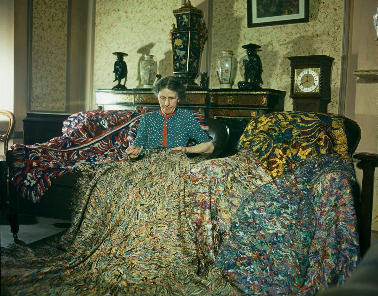 A person sits on a colorful, textured sofa with ornate decorations and vases behind them.