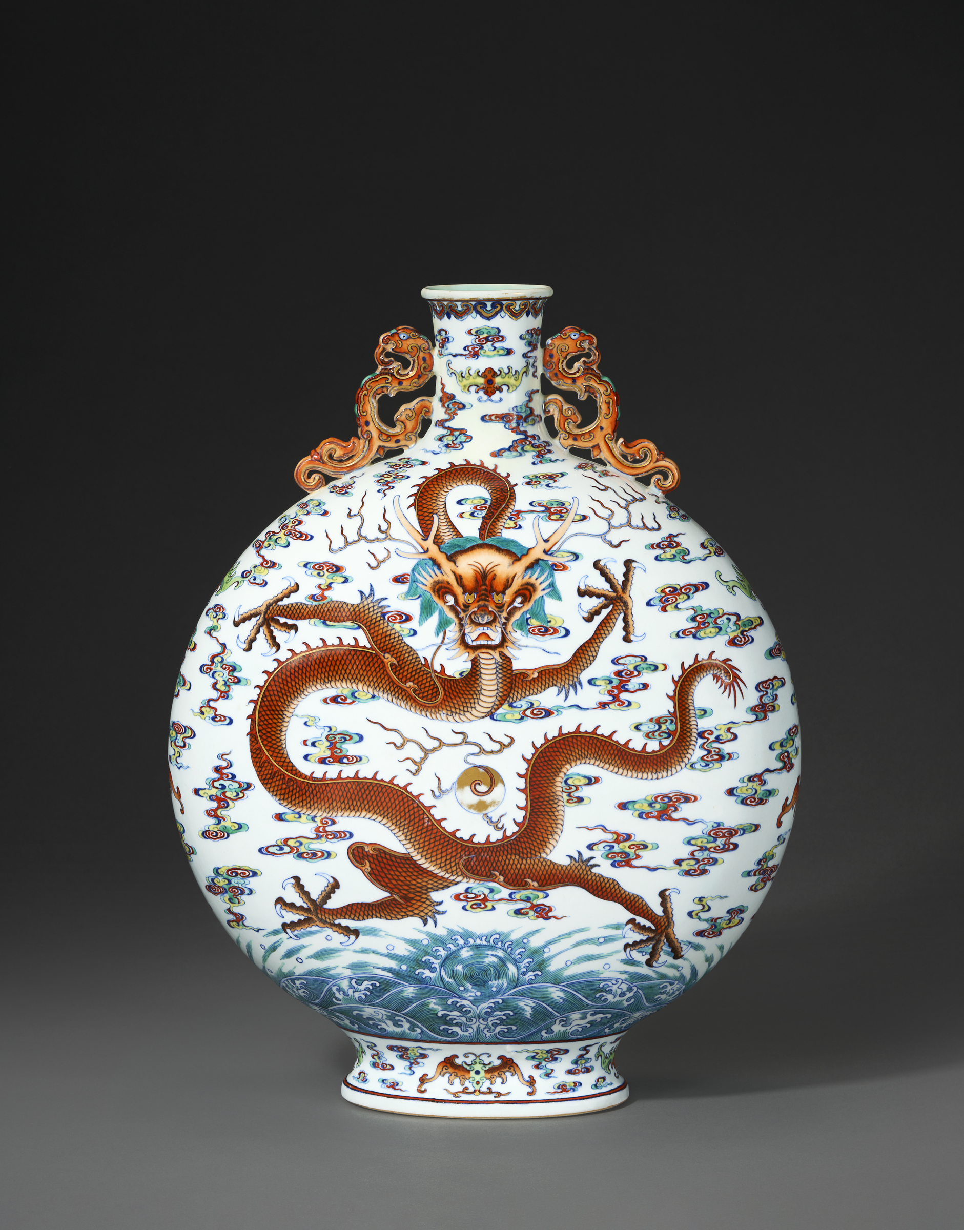 A round porcelain vase with a dragon motif and ornate handles on a dark background.
