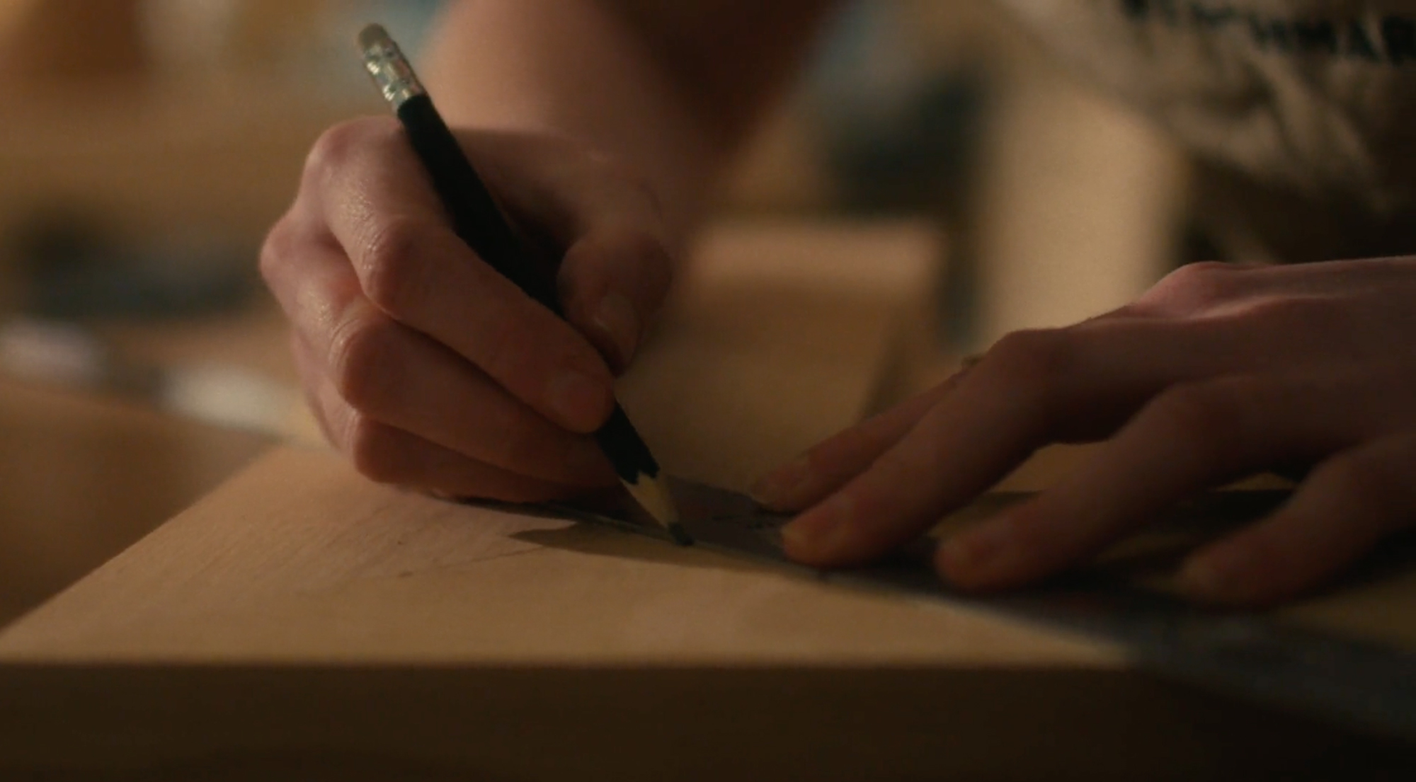 A person is marking wood with a pencil and ruler.