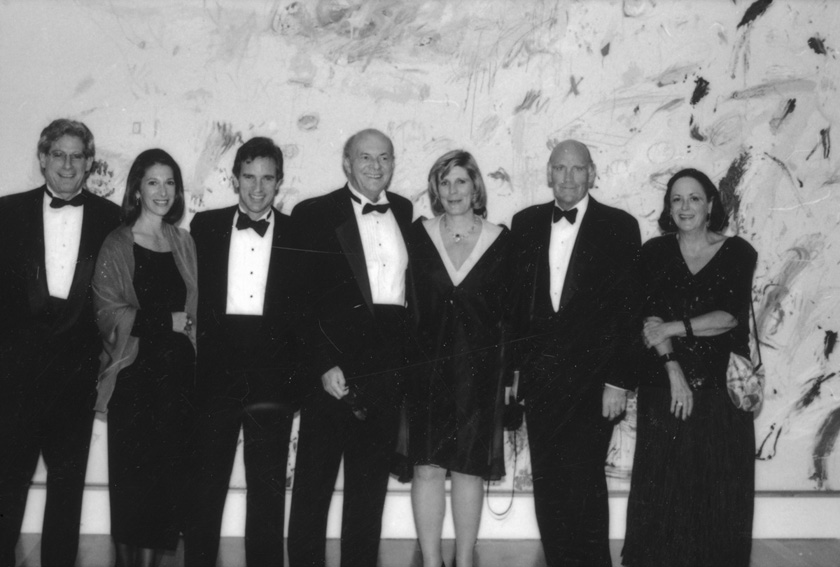 A group of people dressed formally stand together in front of an abstract art wall.