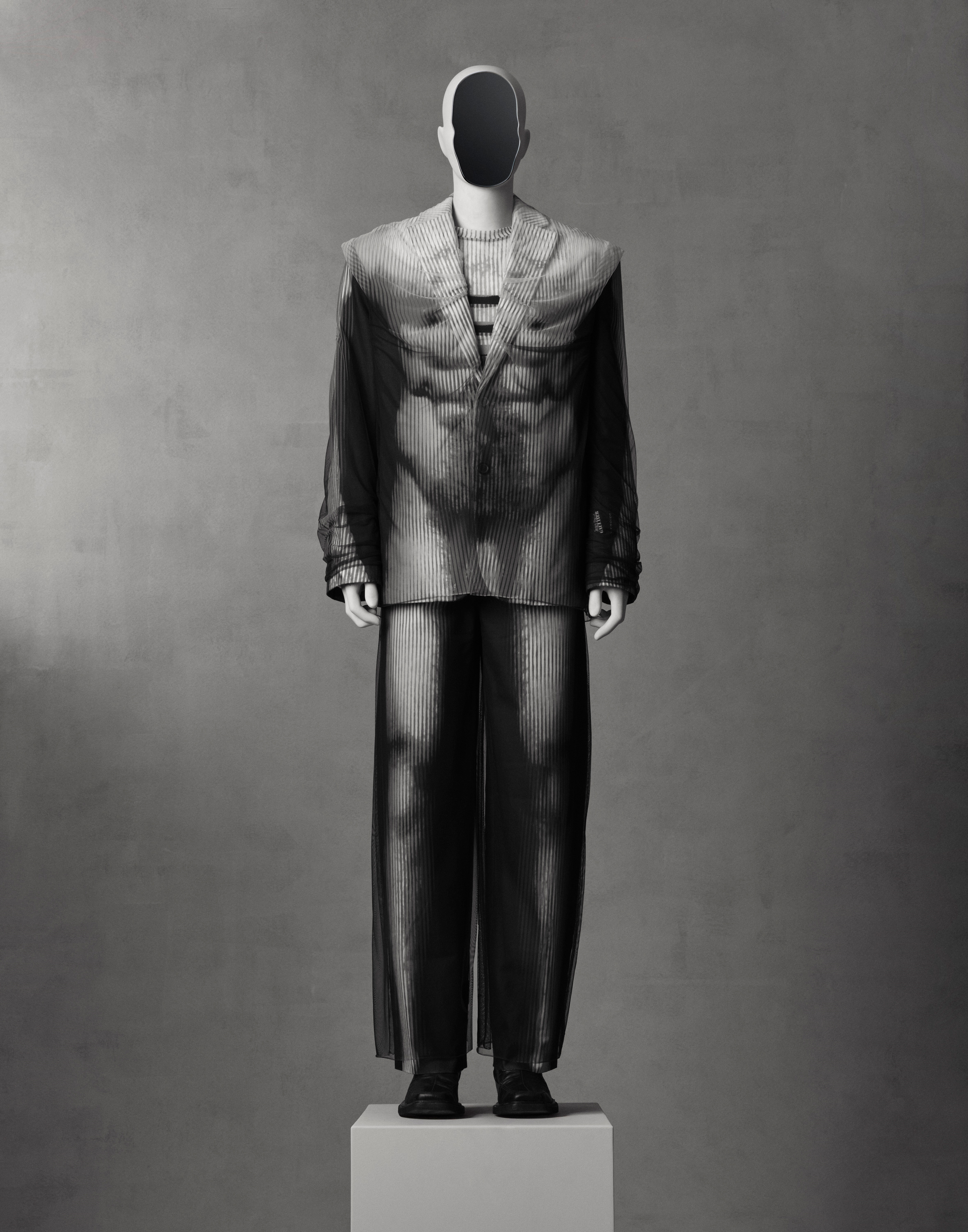 A mannequin wears a striped, translucent suit with broad shoulders and wide-legged pants.