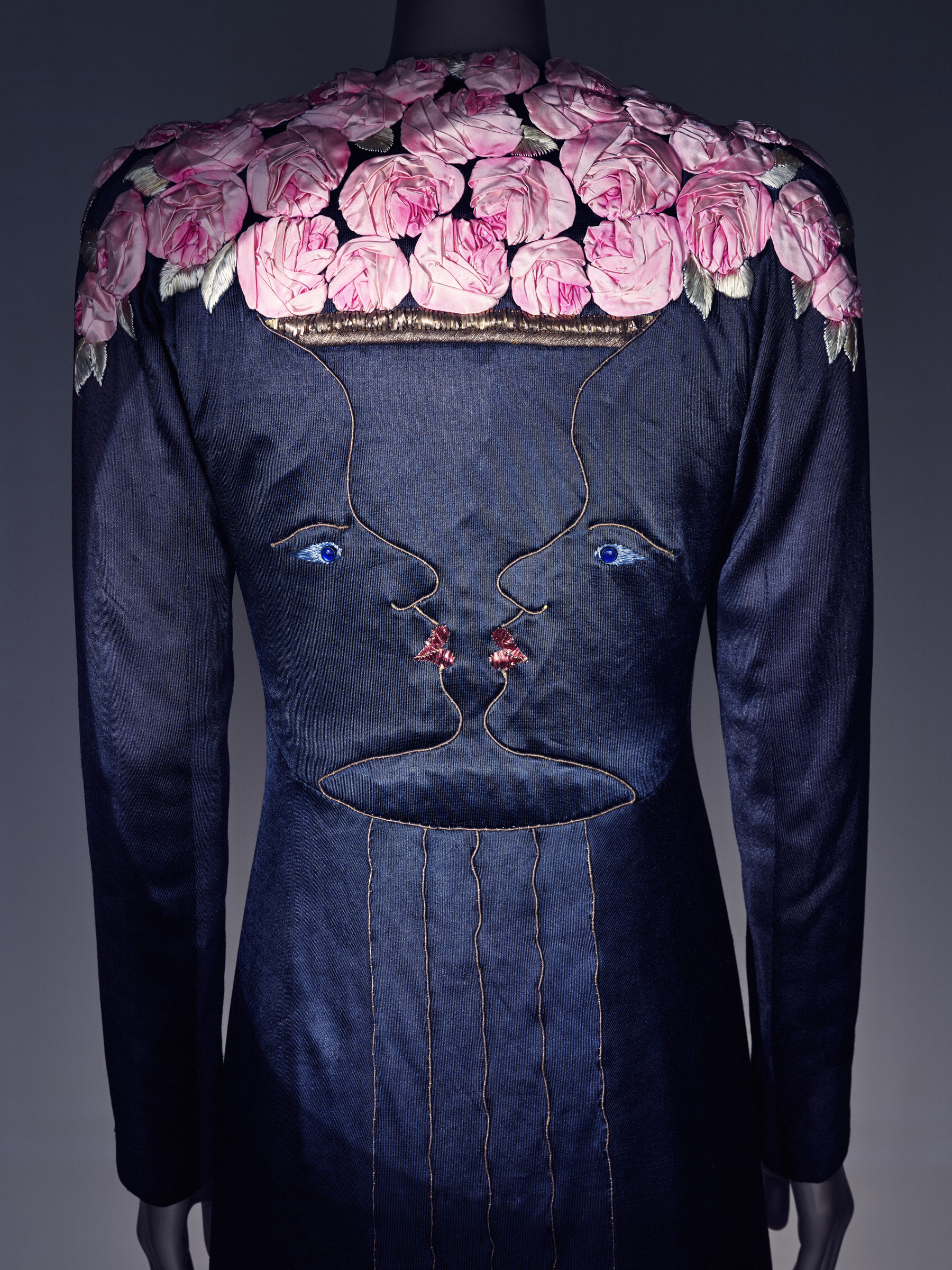 A dark dress features pink flower embellishments and a surreal embroidered face design on the back.