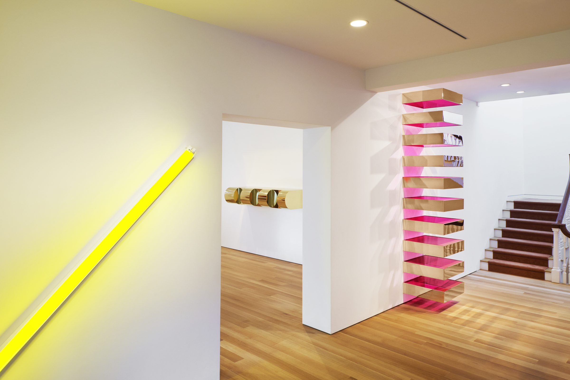 Modern interior with wooden floors, neon yellow light, floating shelves, and wall-mounted art.