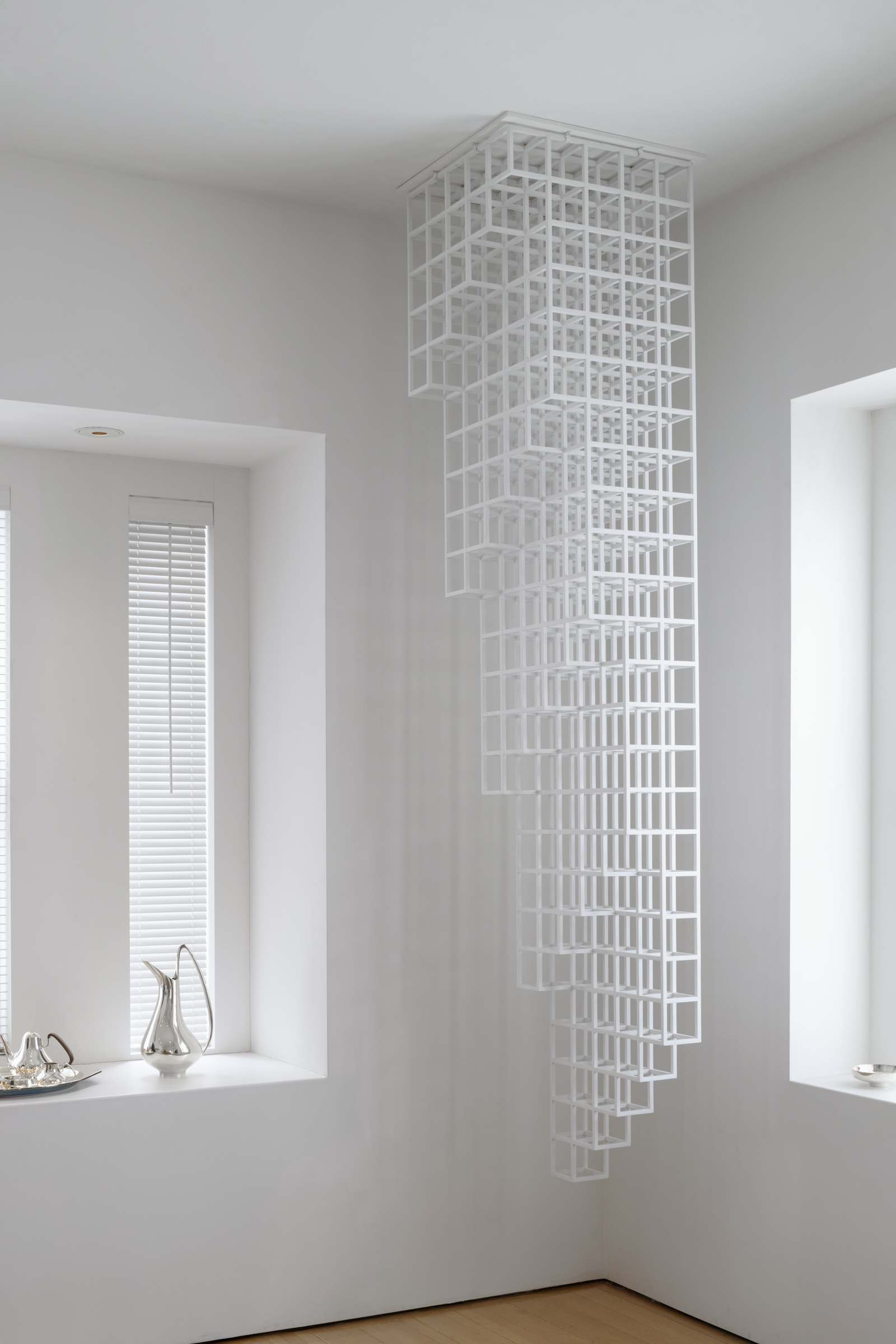 A geometric white grid sculpture hangs from the ceiling in a minimal, modern room.