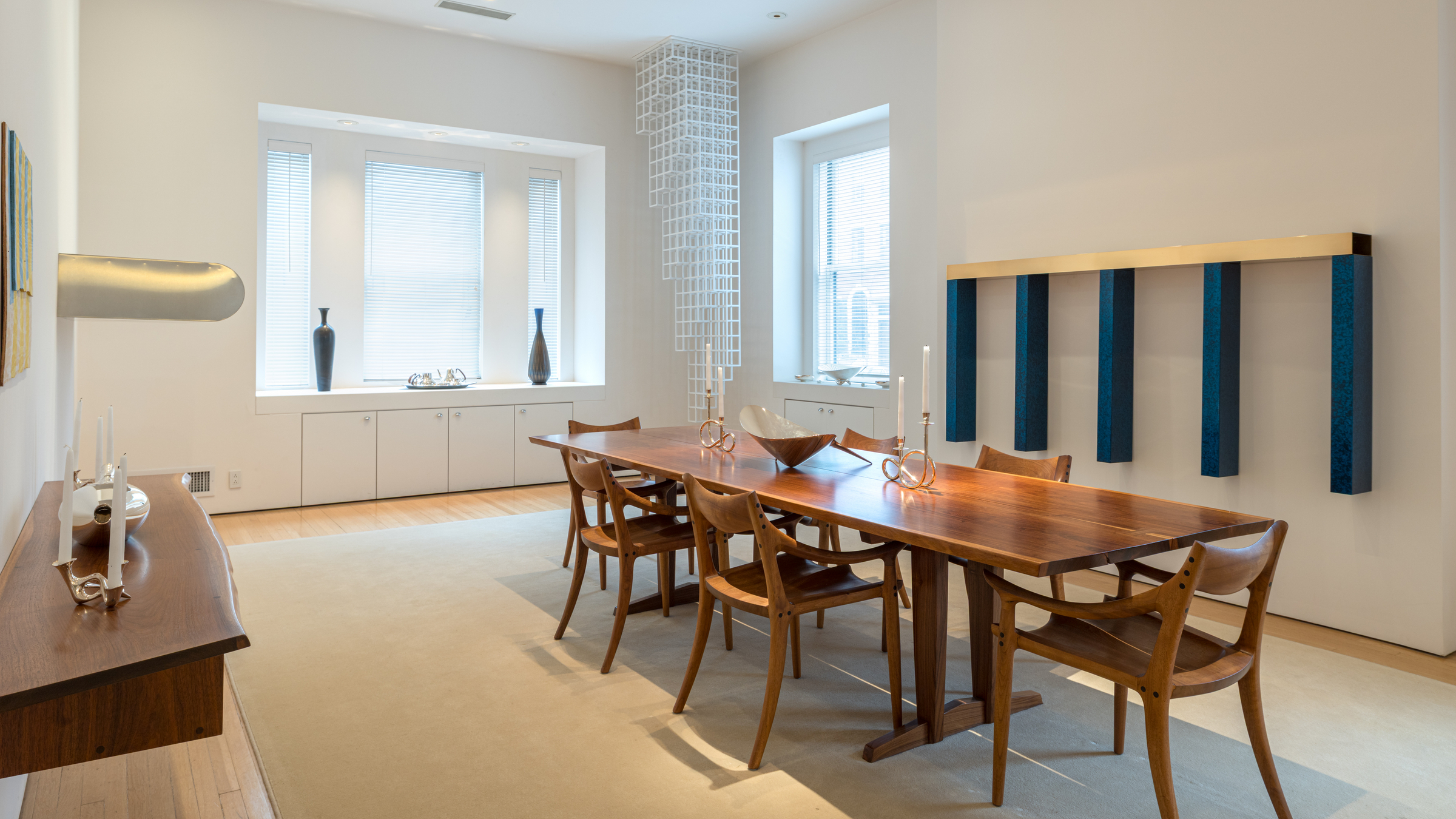 A modern dining room with a wooden table, six chairs, minimalist decor, and large windows.