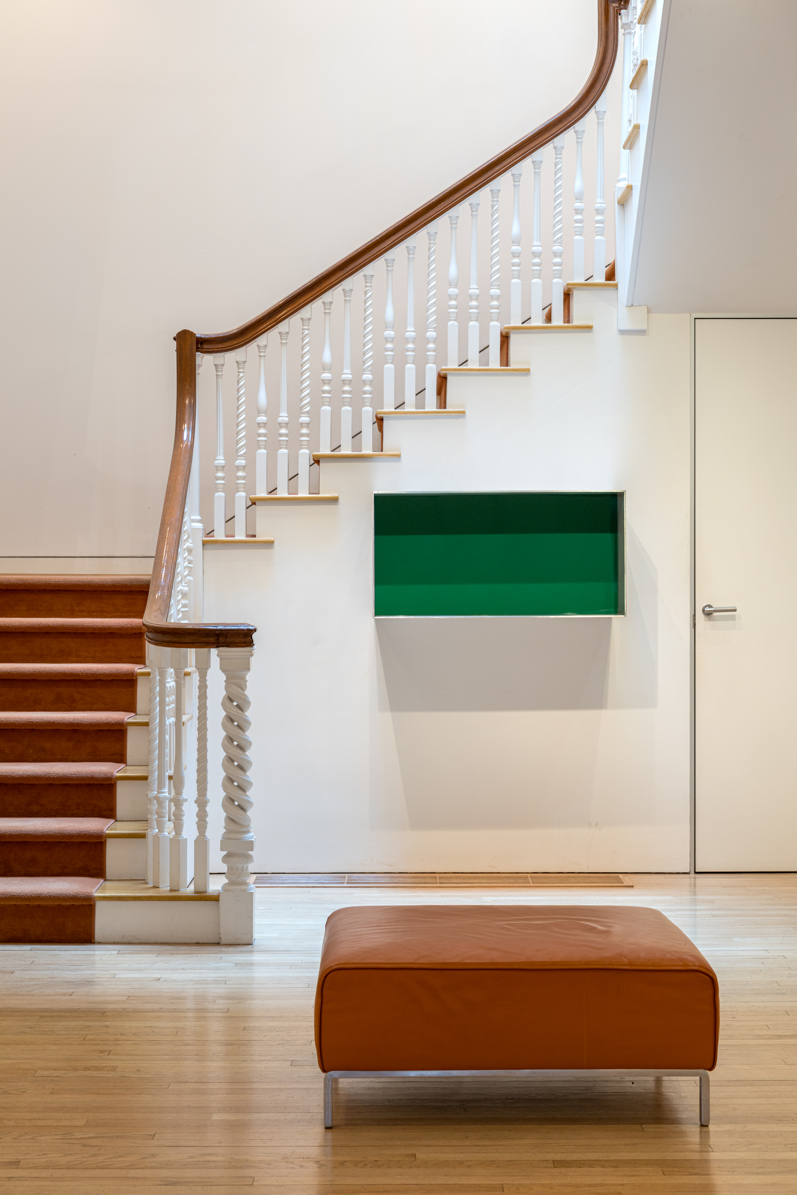A modern interior with a staircase, green wall shelf, and an orange ottoman.