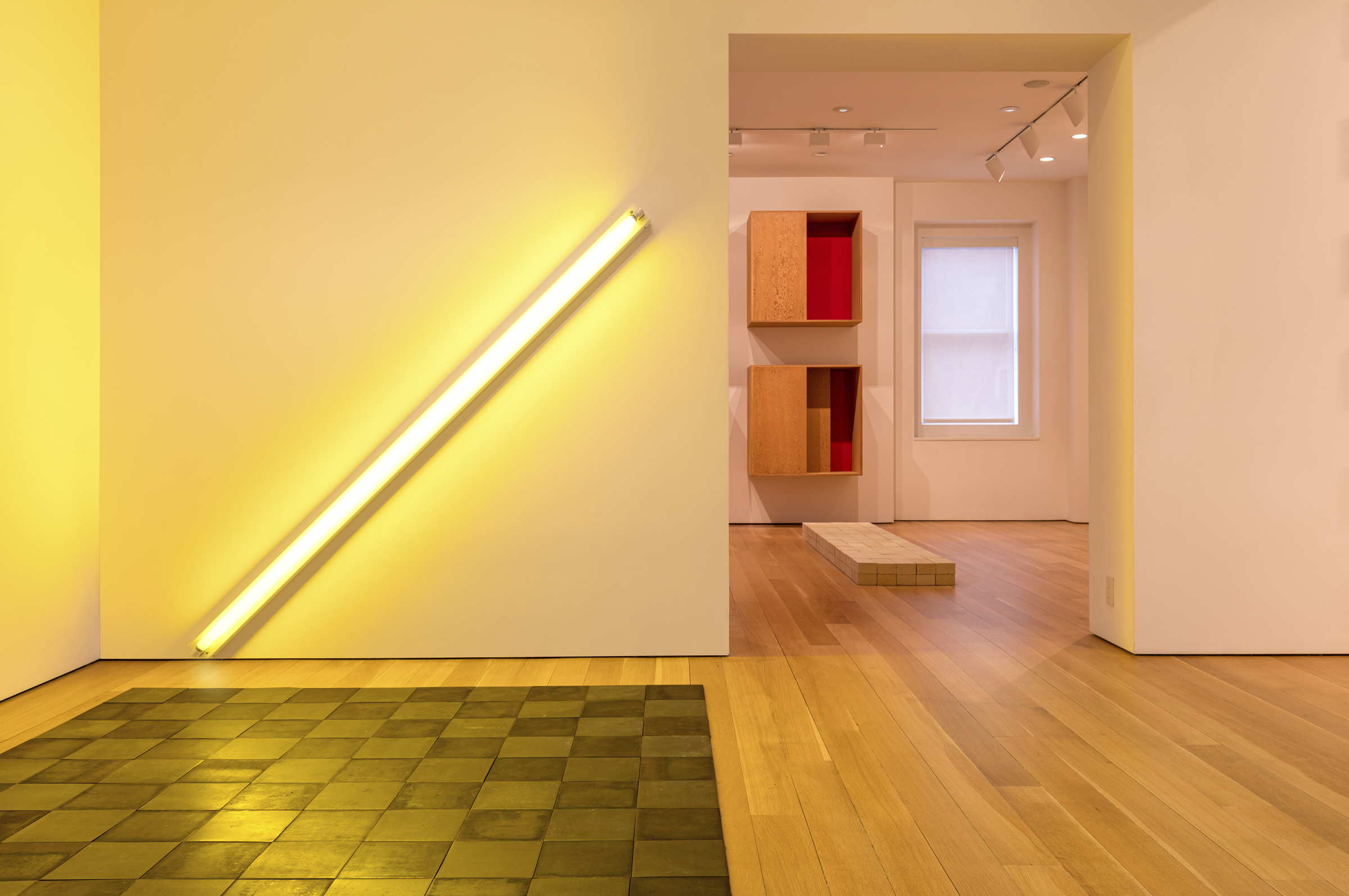 A modern art gallery with minimalist decor, featuring a diagonal yellow light and geometric objects.