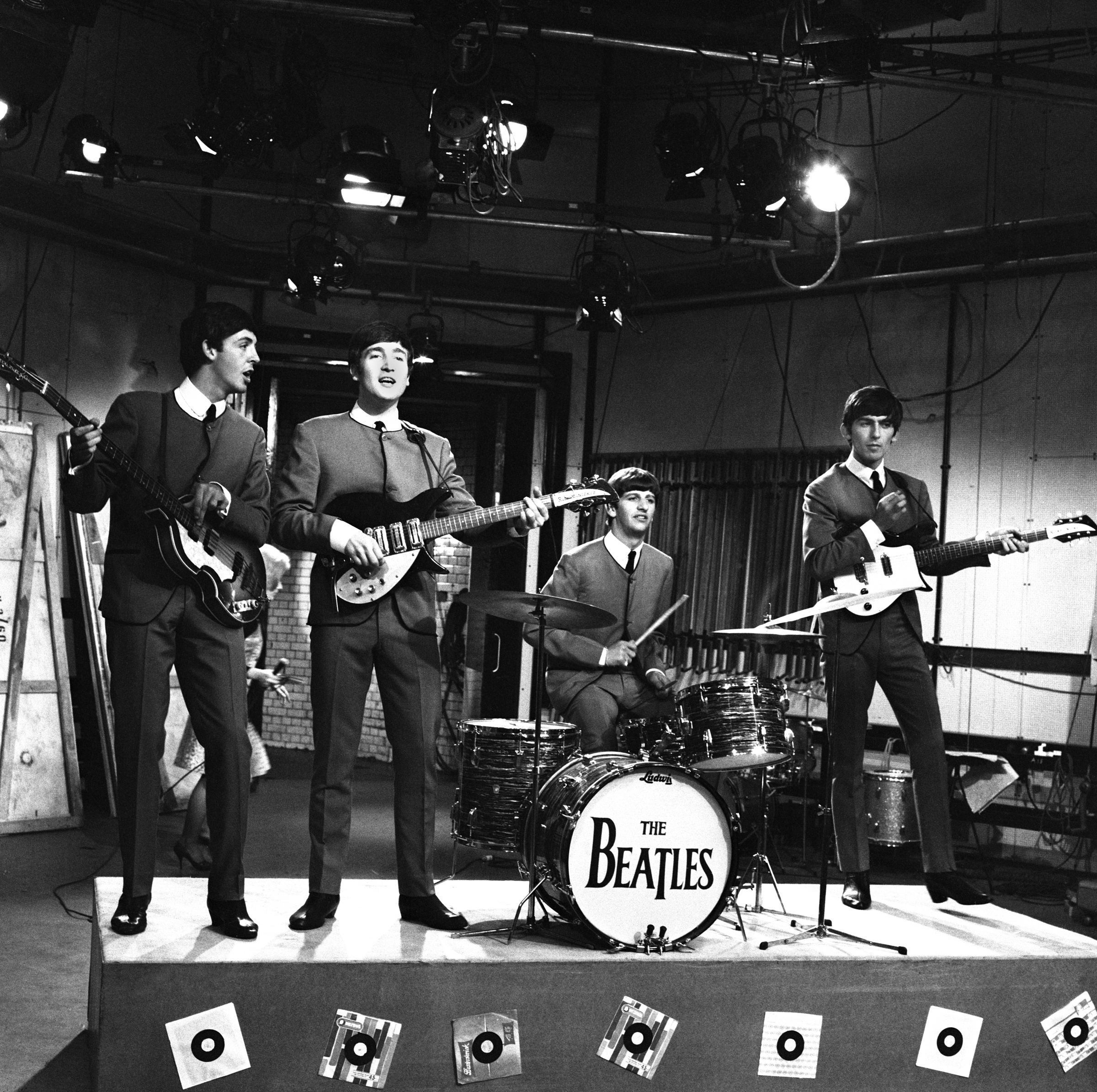 A band is performing on stage with instruments, and "The Beatles" is written on the drum.