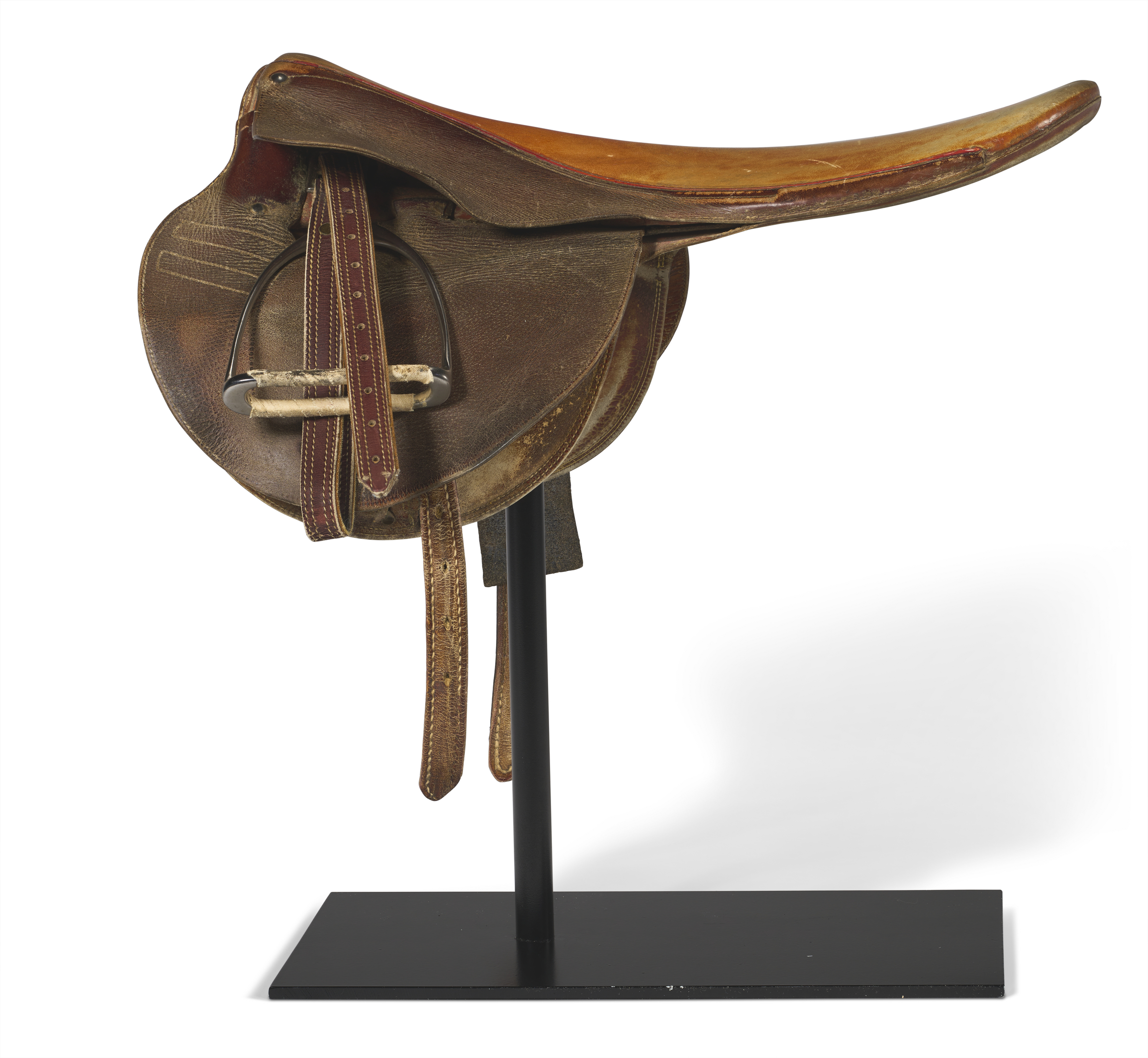 A vintage leather horse saddle with stirrups displayed on a black stand.