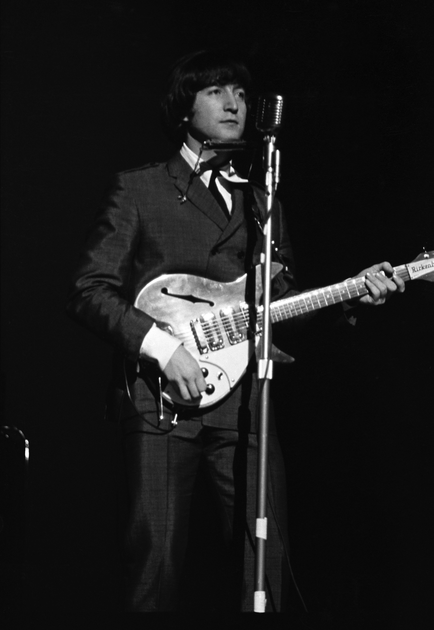A person in a suit is playing an electric guitar and standing in front of a microphone.