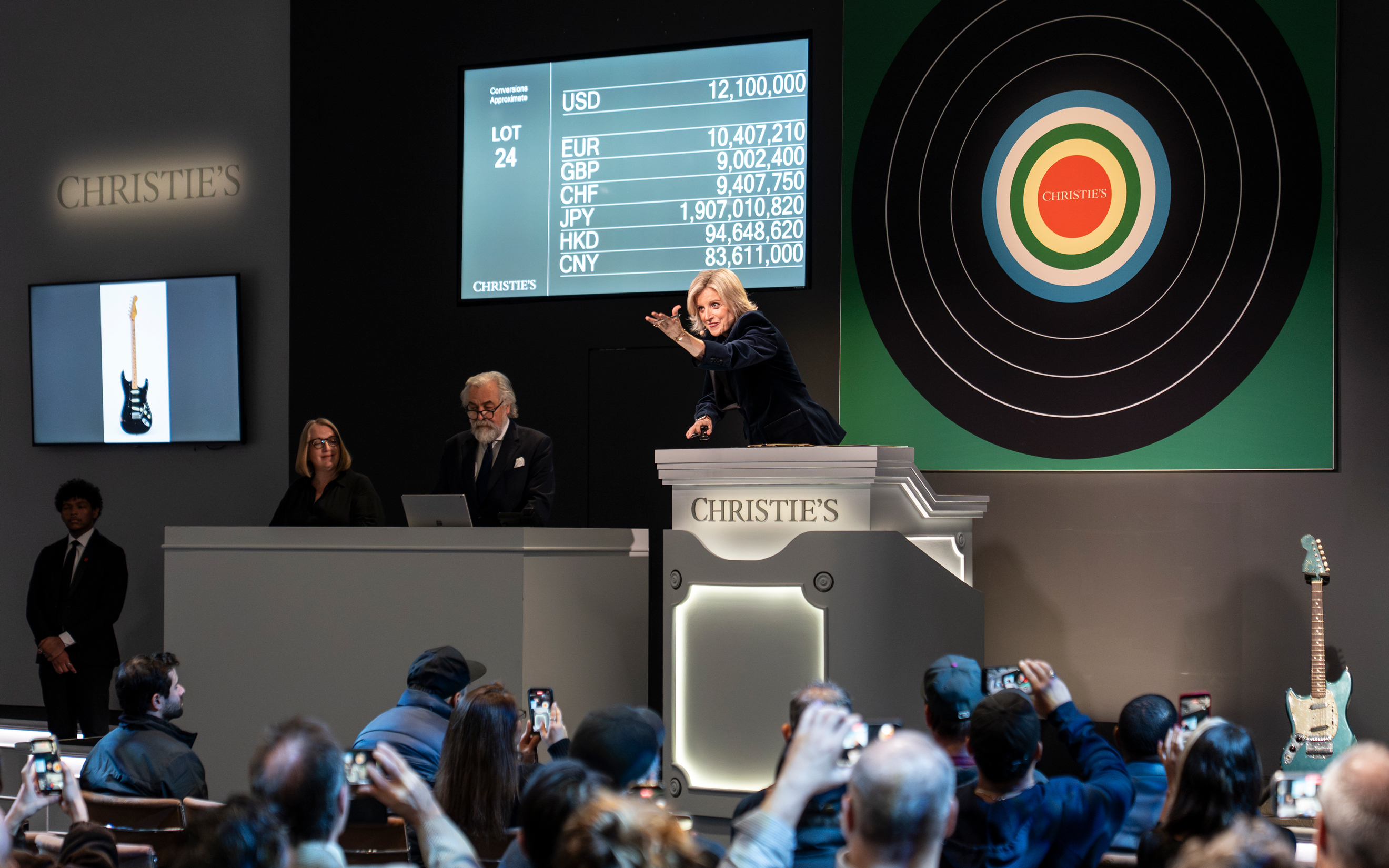An auction is taking place at Christie's with a guitar as the featured item and people bidding.