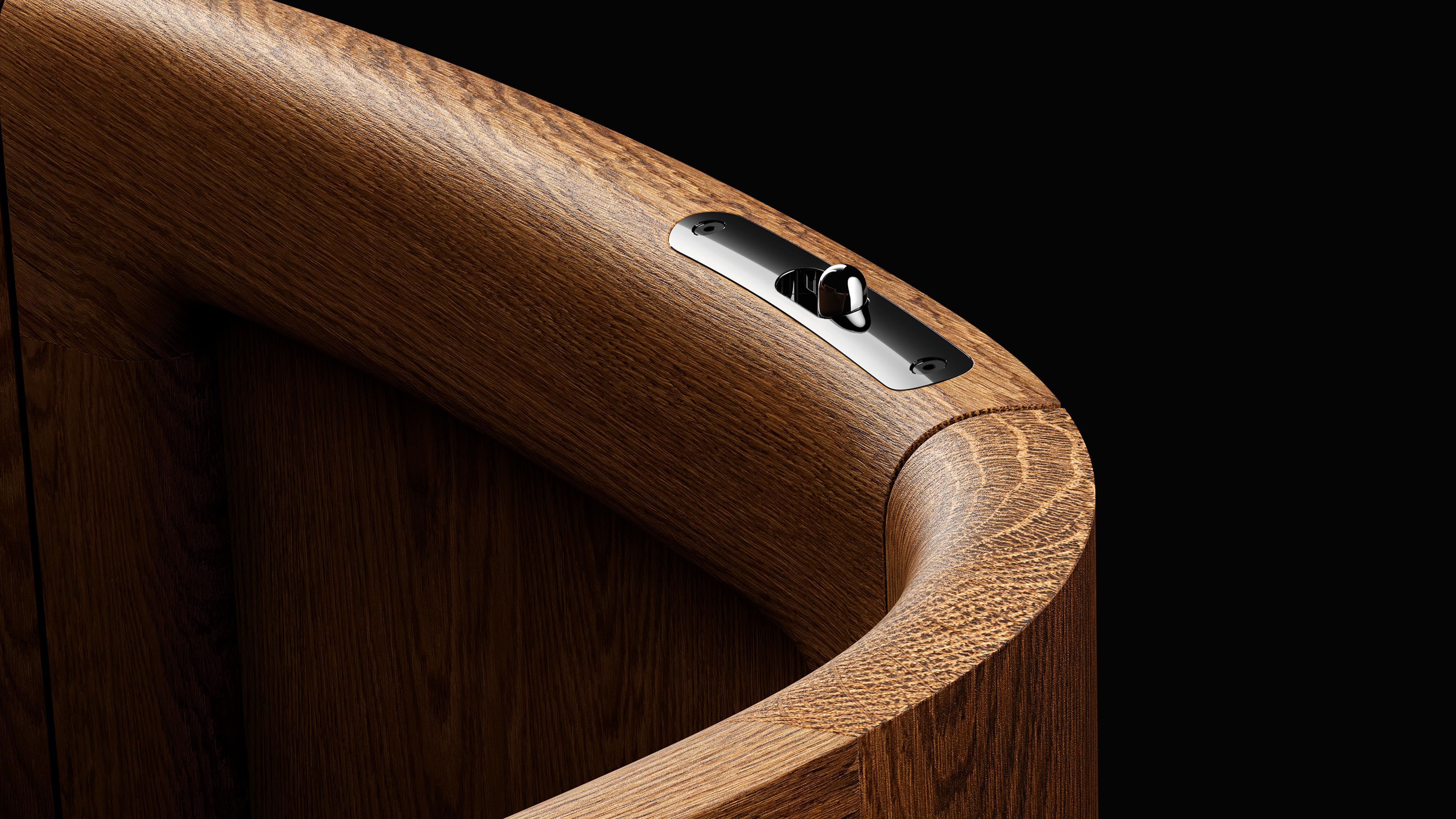 Curved wooden surface with a sleek metal fixture against a black background.