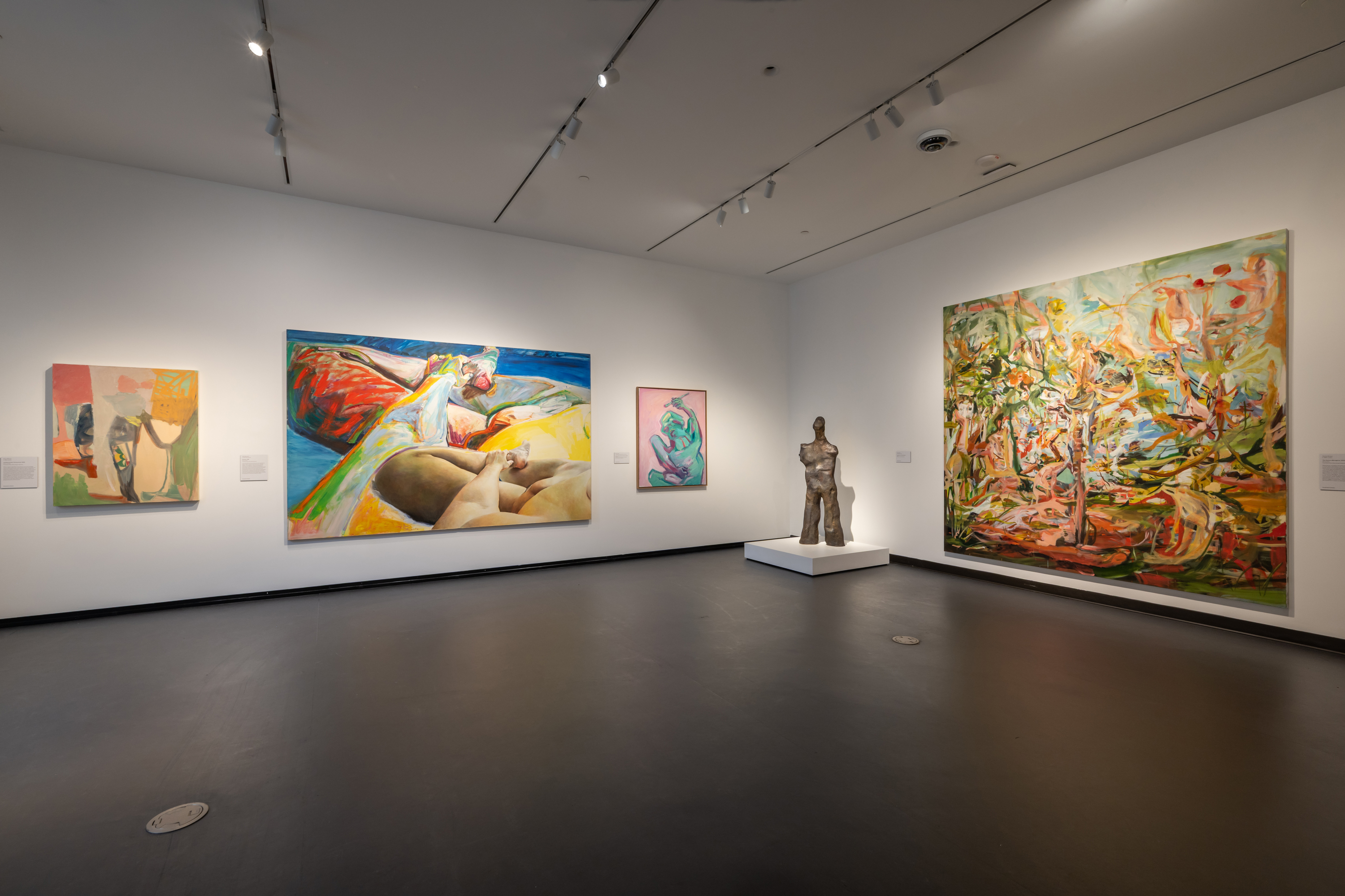 A modern art gallery room with colorful abstract paintings and a central human torso sculpture.