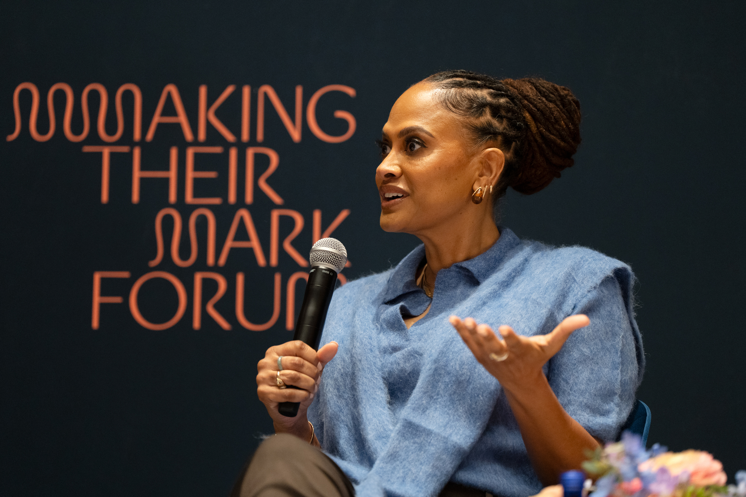 A person is speaking into a microphone at the "Making Their Mark Forum" event.
