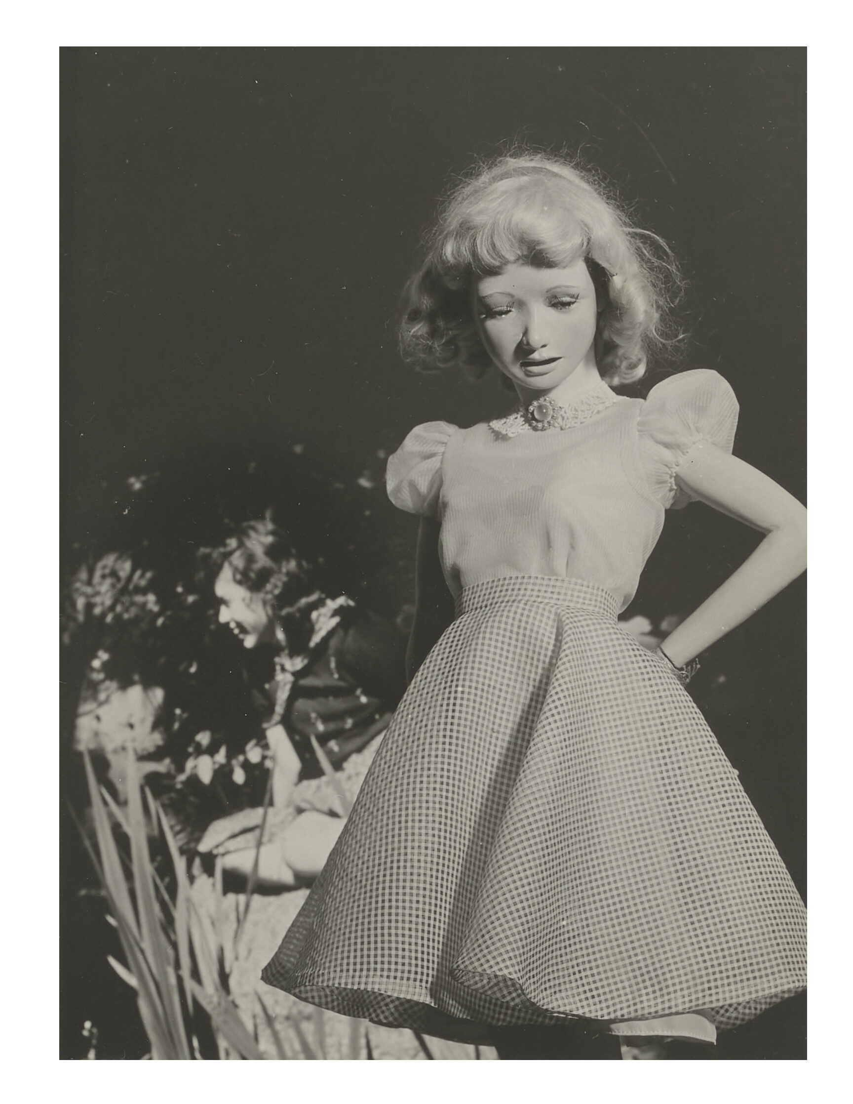 A girl in a checkered skirt and puffed sleeve blouse stands outdoors with her face blurred.