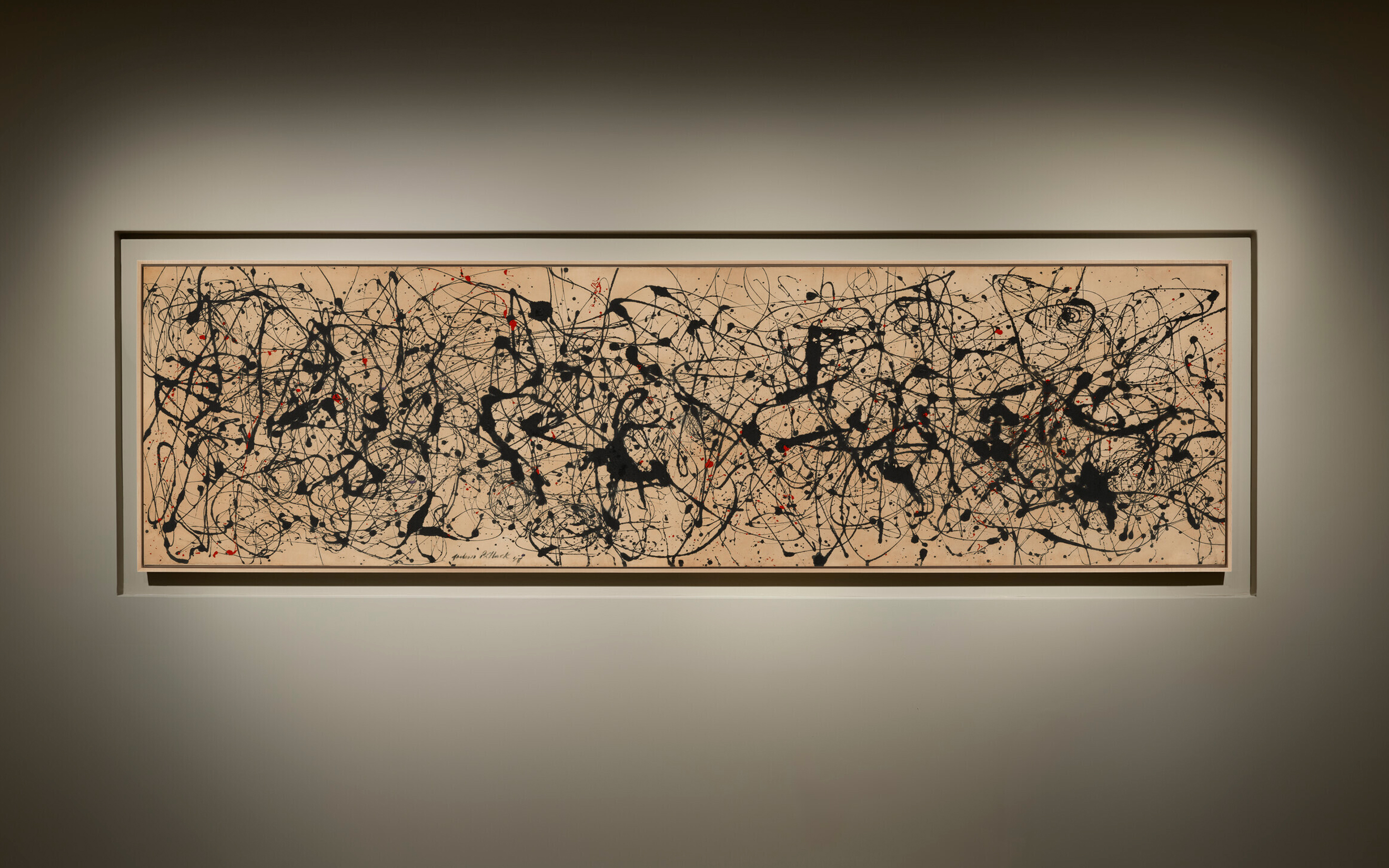 A long abstract painting with black and red splatters and lines on a tan background.