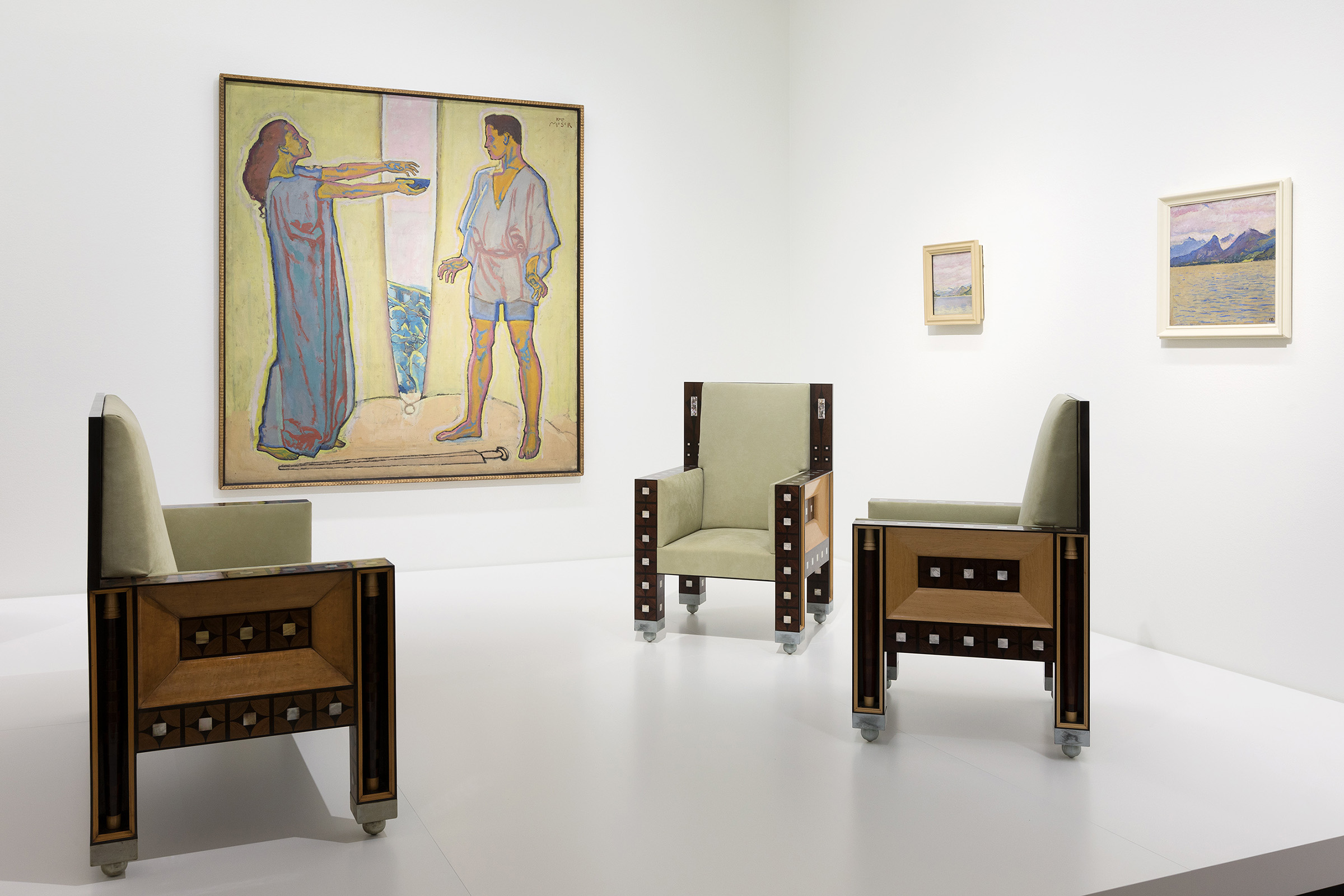 An installation view of the Leopold Museum's ongoing exhibition Vienna 1900. Birth of Modernism, which opened in 2019. The armchairs, dating from 1913, were designed by Koloman Moser, who also painted the three works on the walls, from left: Der Liebestrank (Tristan und Isolde), 1913-15; Wolfgangsee mit tiefem Horizont (Wolfgangsee with Low Horizon), circa 1913; and Wolfgangsee, circa 1913