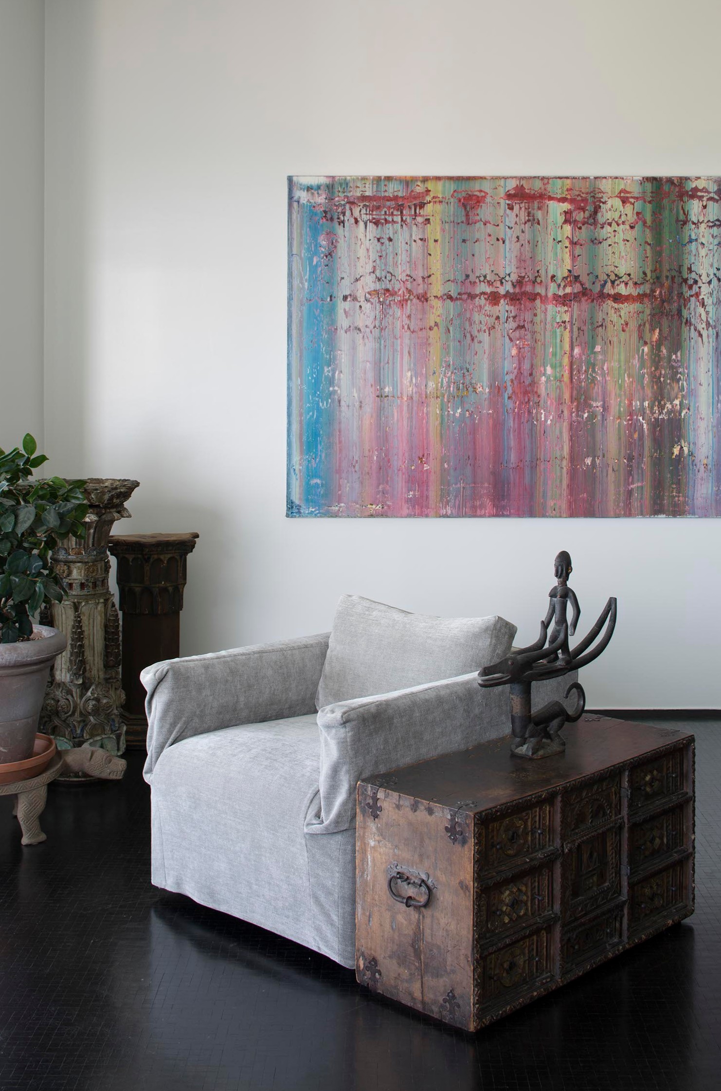 A cozy armchair sits next to a rustic wooden chest, with abstract art and plants in the background.