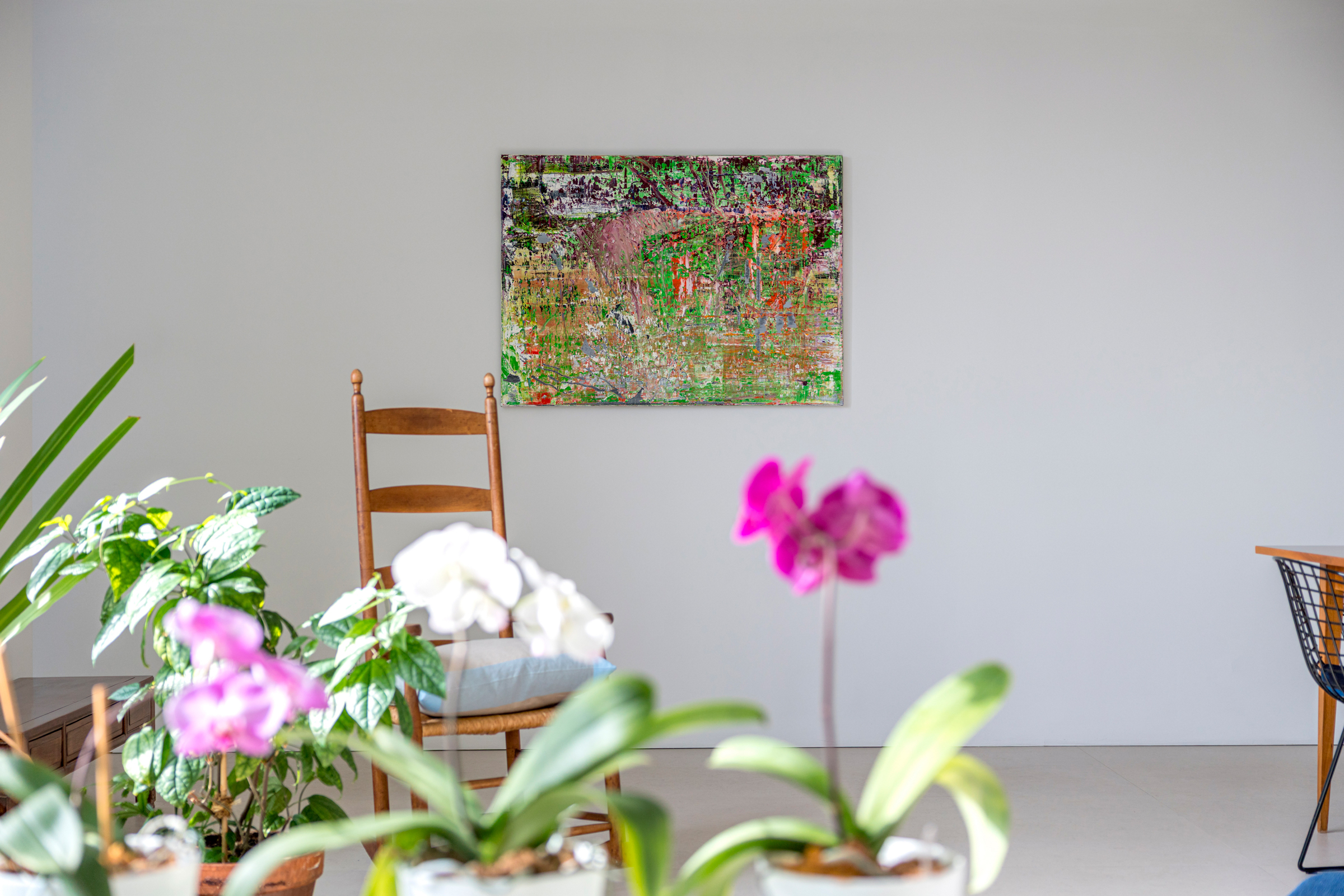 A bright room with potted plants, a wooden chair, and an abstract painting on the wall.
