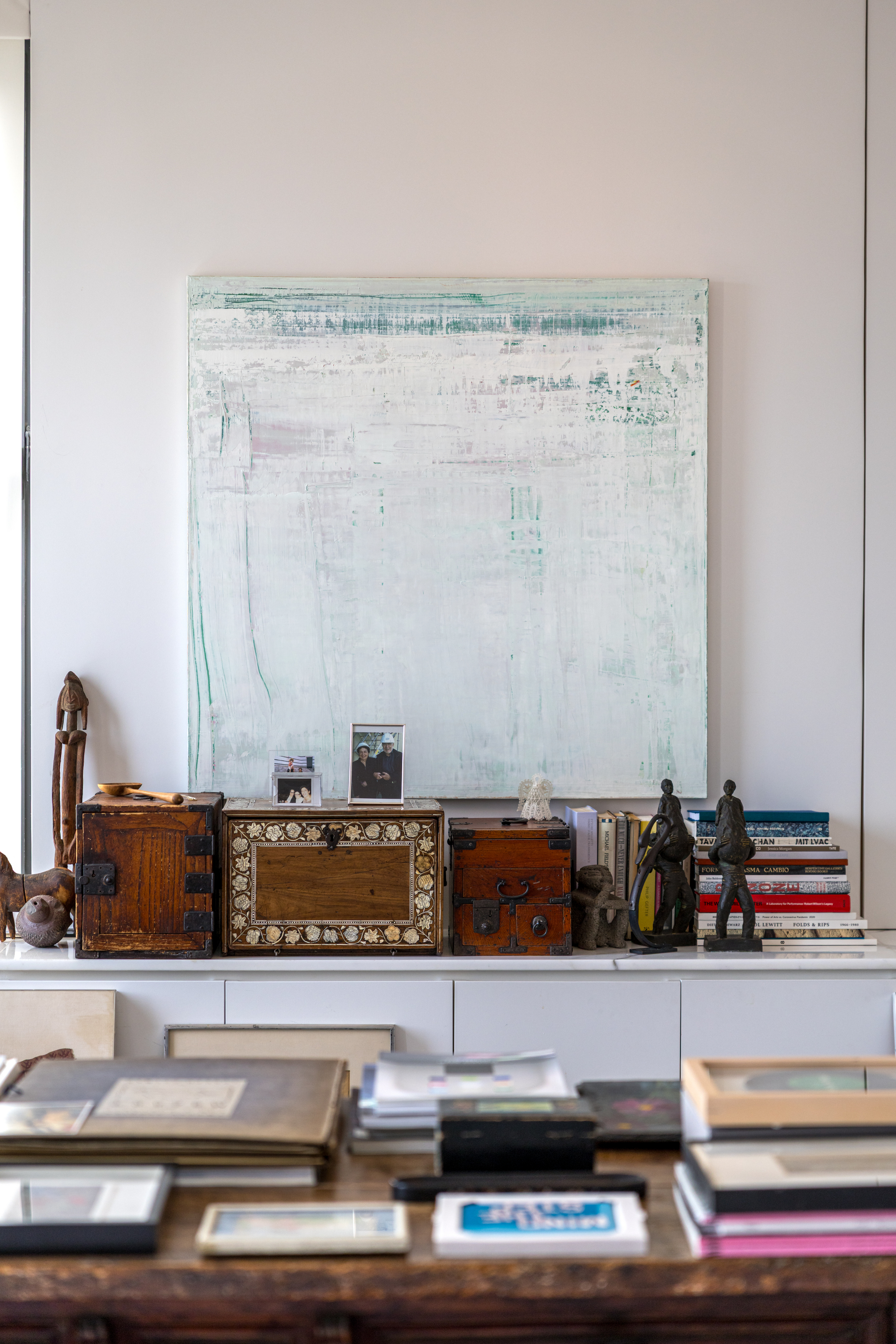 A shelf with books, decorative chests, figurines, and a large abstract painting on the wall.