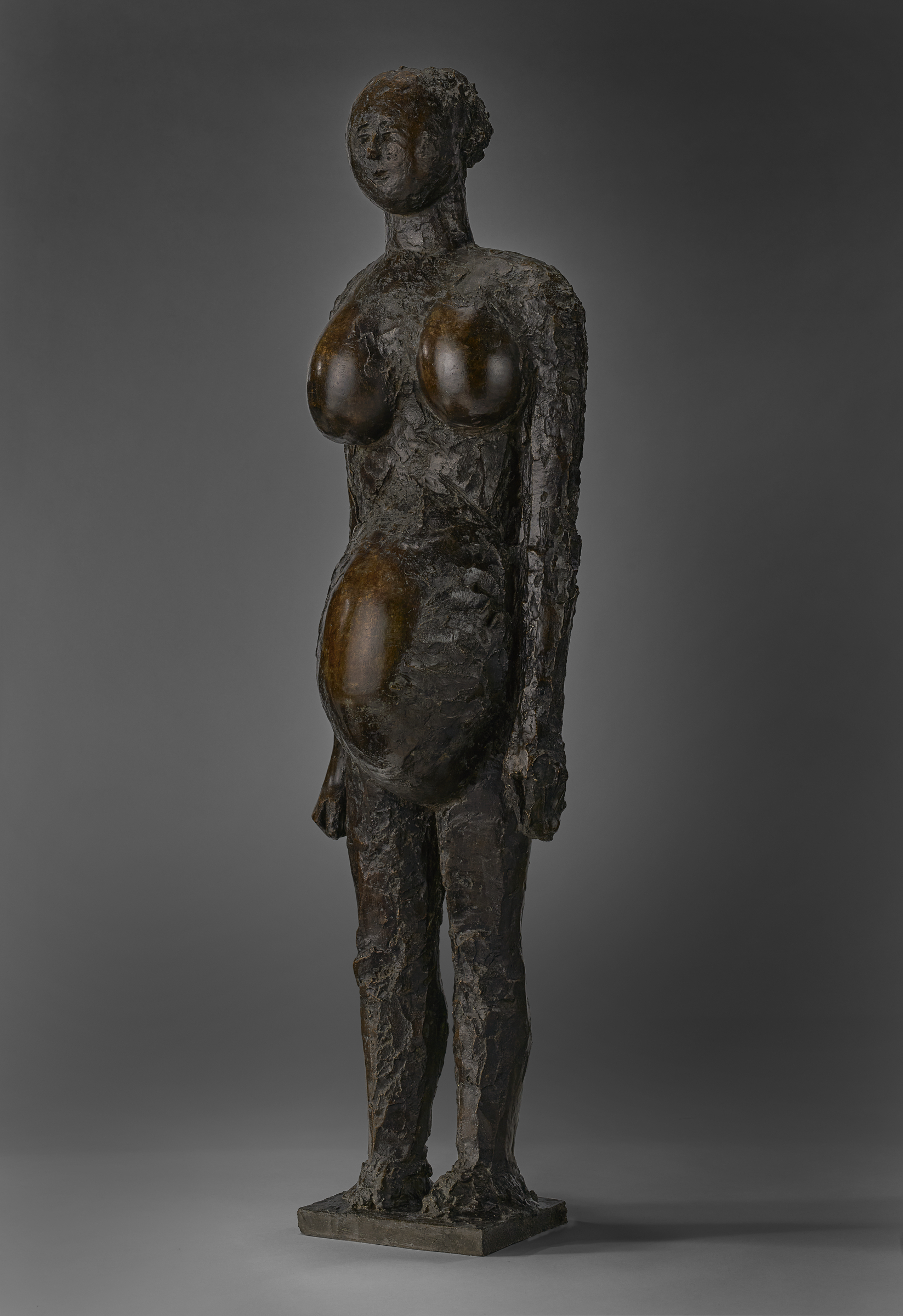 A bronze sculpture of a standing, abstract female figure with an elongated form and no facial features.