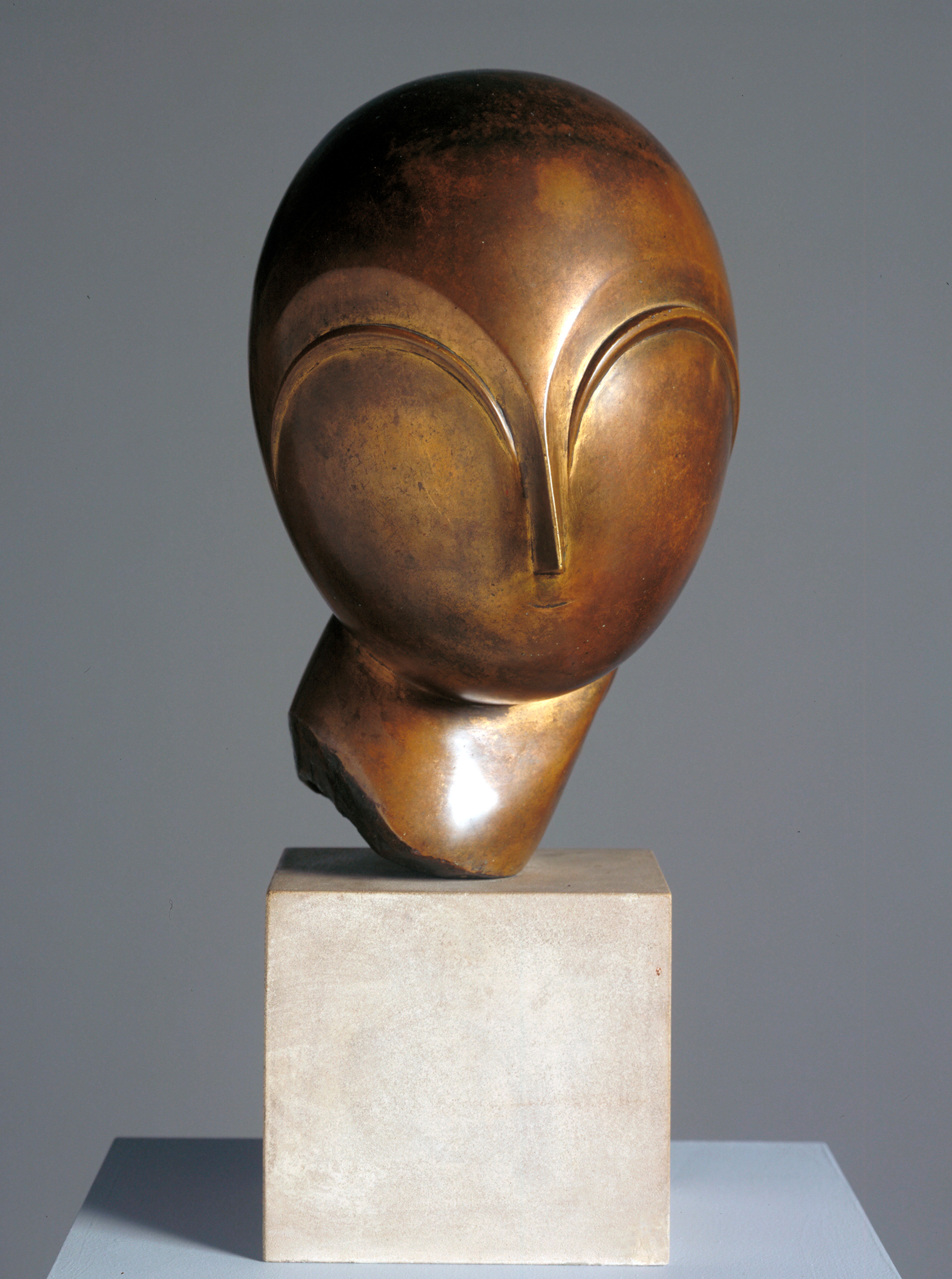 A bronze abstract head sculpture with smooth, minimalist features set on a stone pedestal.